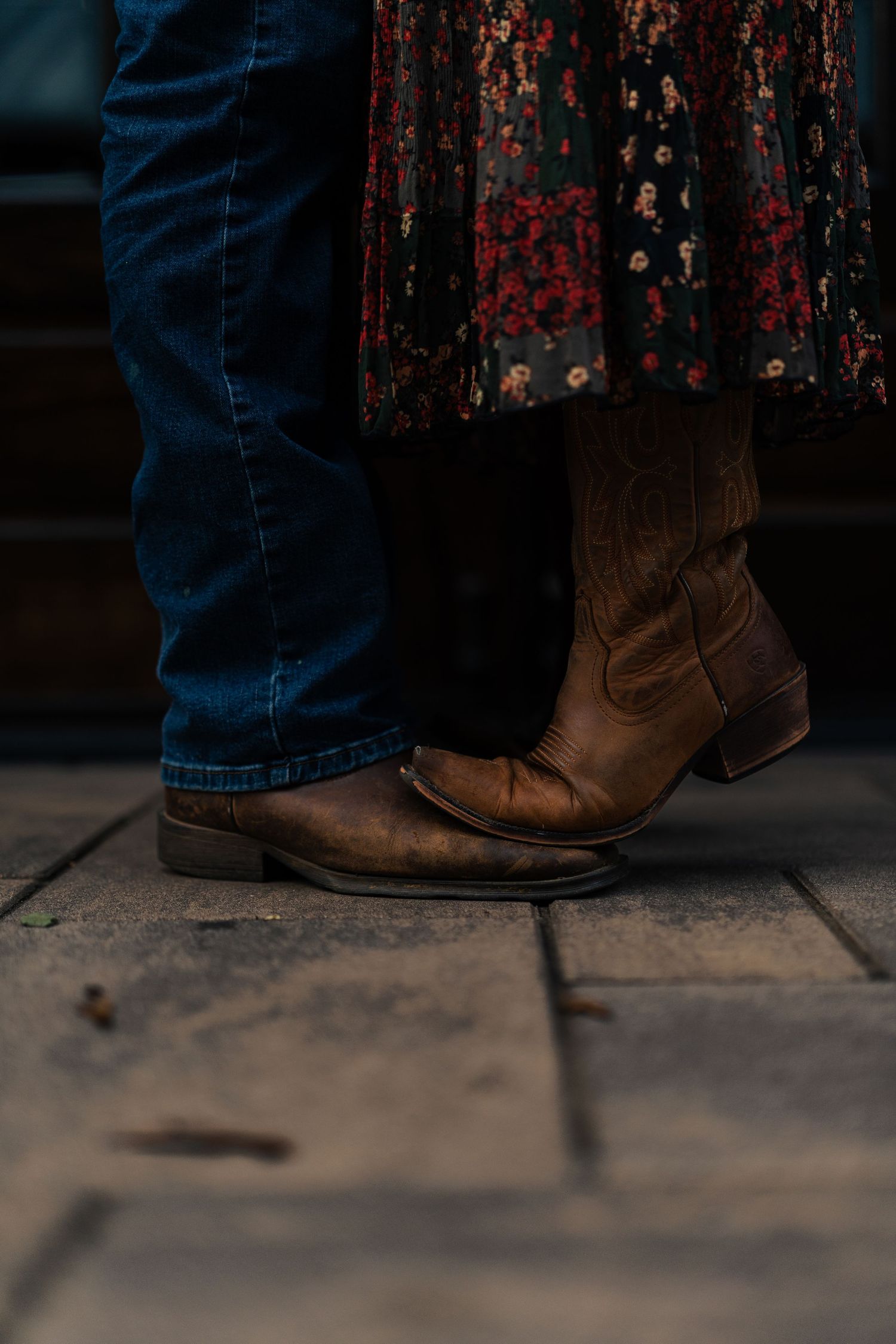 Close-up of brown leather cowboy boots and jeans against a dark textured background.