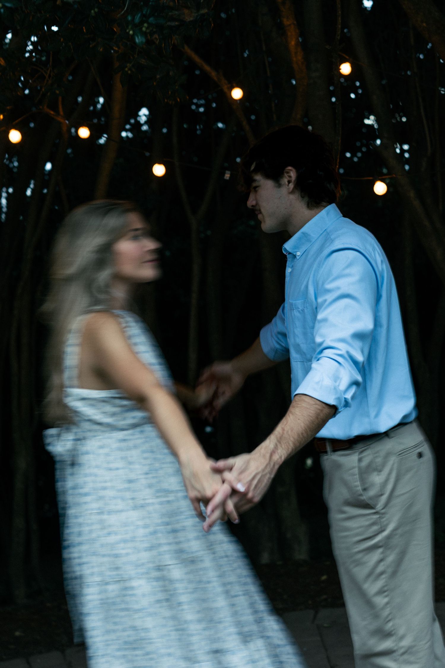 Dancing couple under string lights at dusk in casual evening attire.