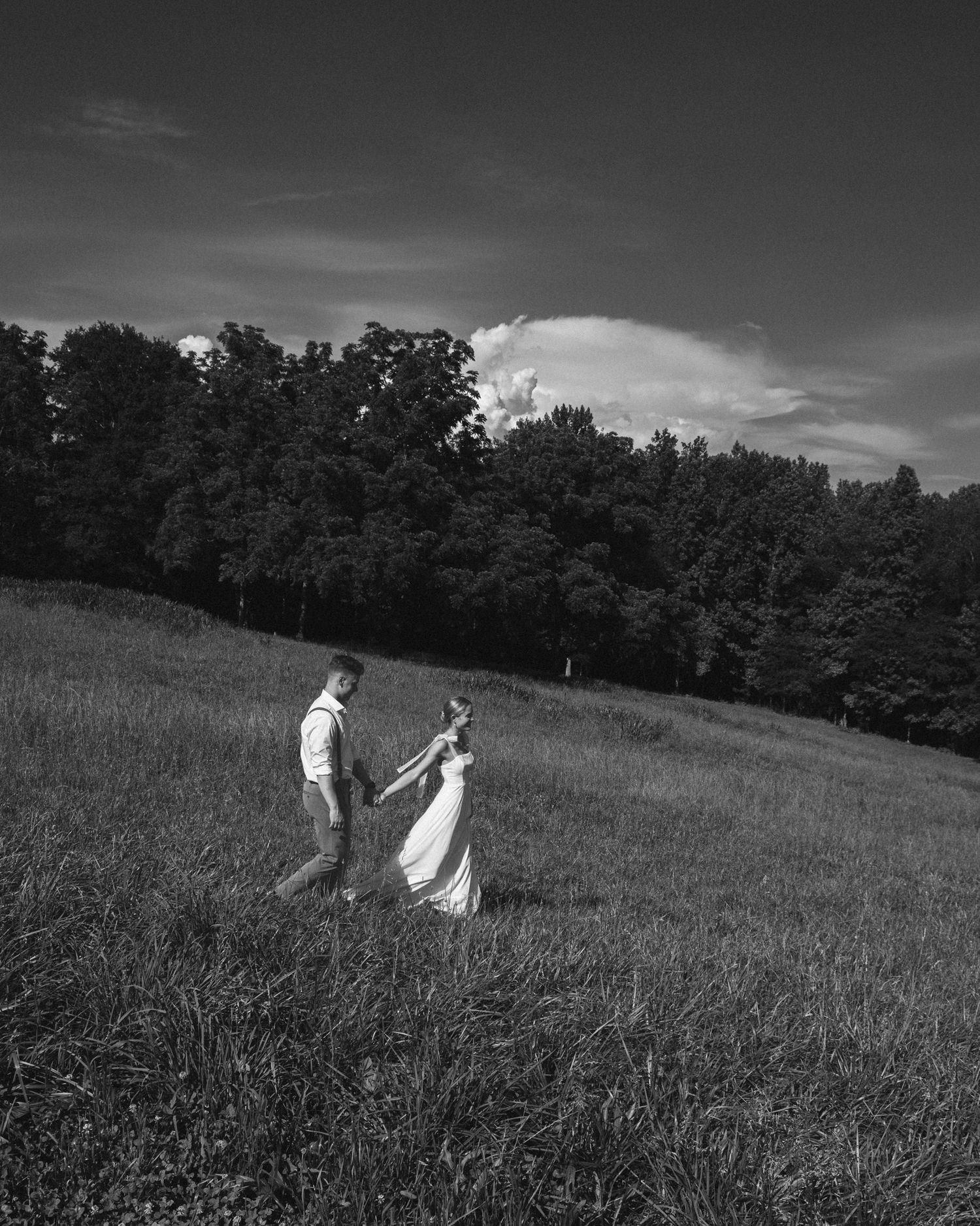 Black and white wedding photography of couple walking through a serene meadow.