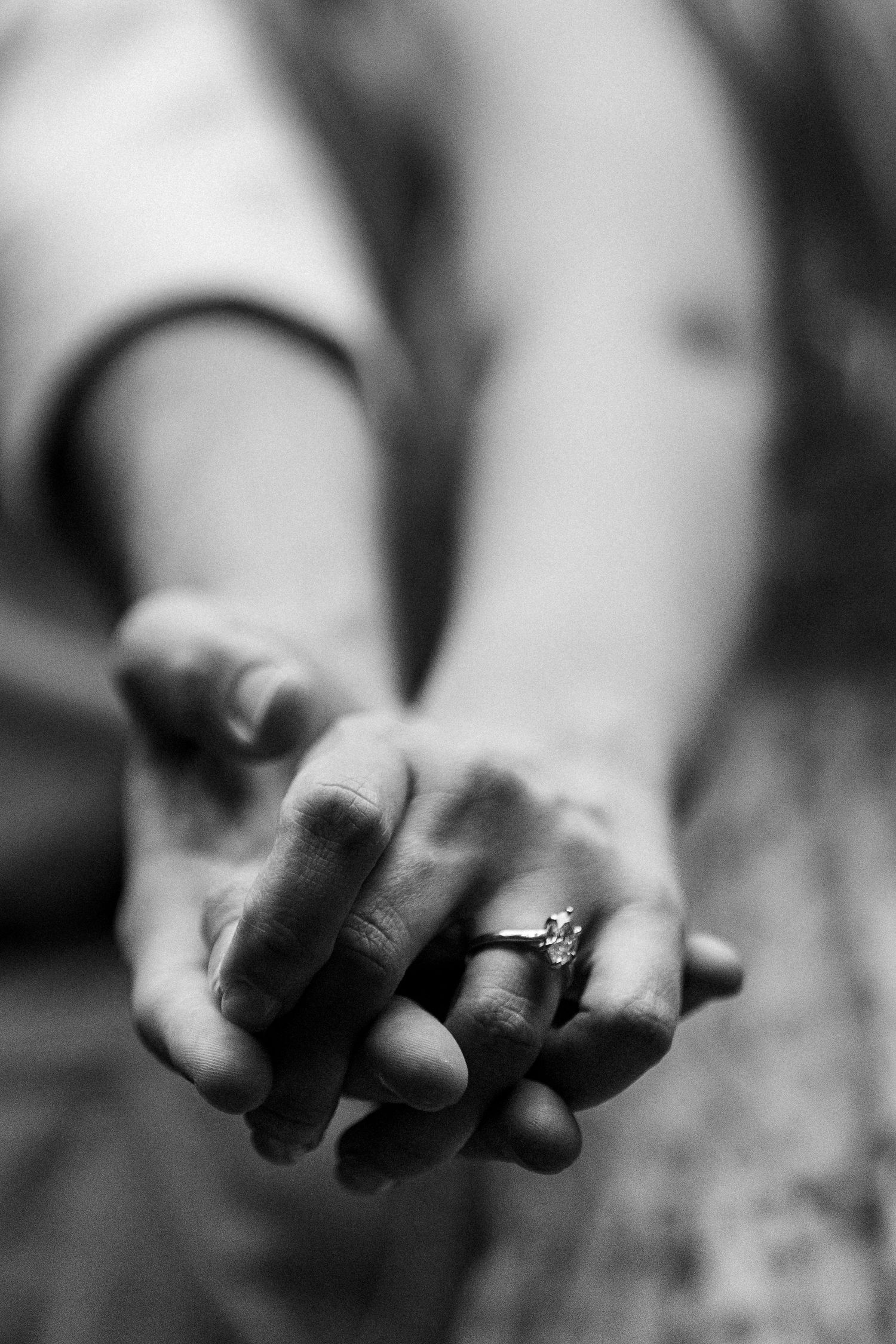 Black and white close-up of clasped hands wearing an engagement ring.