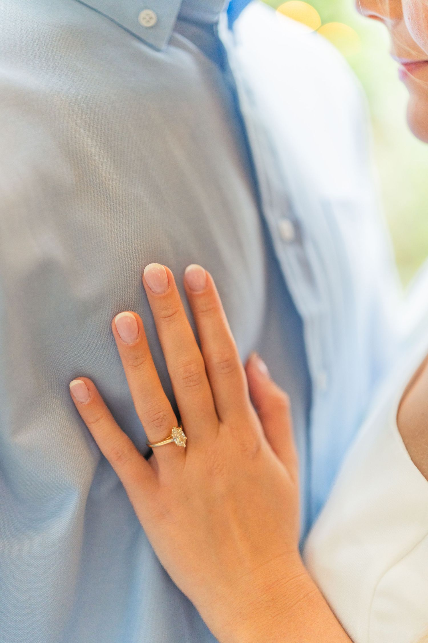 Close-up of hands with a wedding ring resting on light blue fabric.