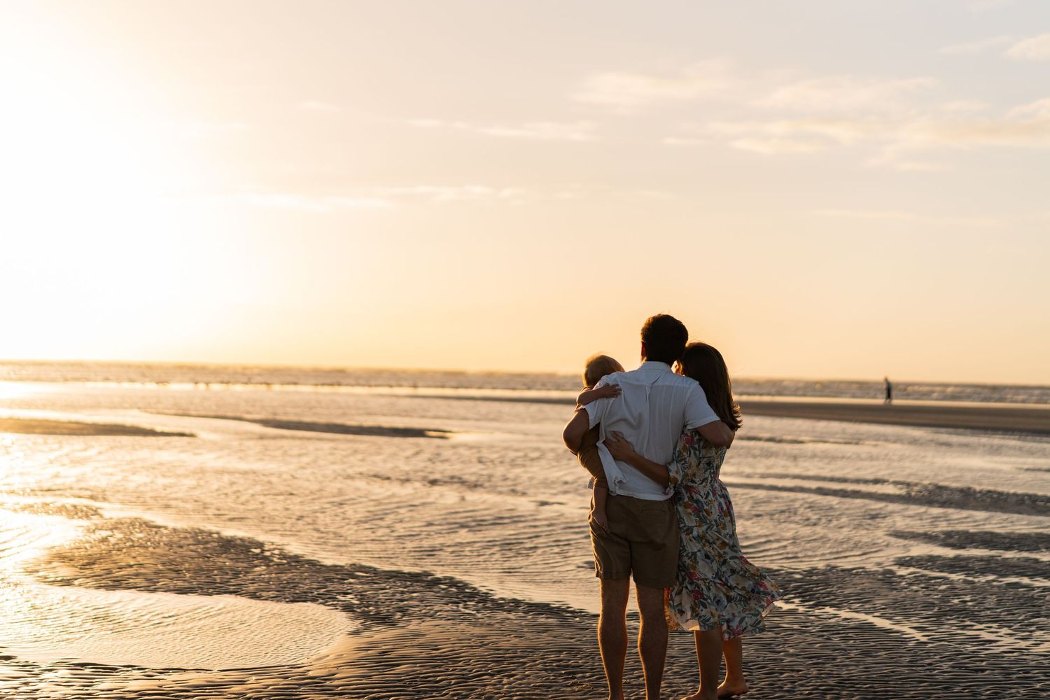 Silhouettes of people walking along the beach shoreline during a golden sunset.