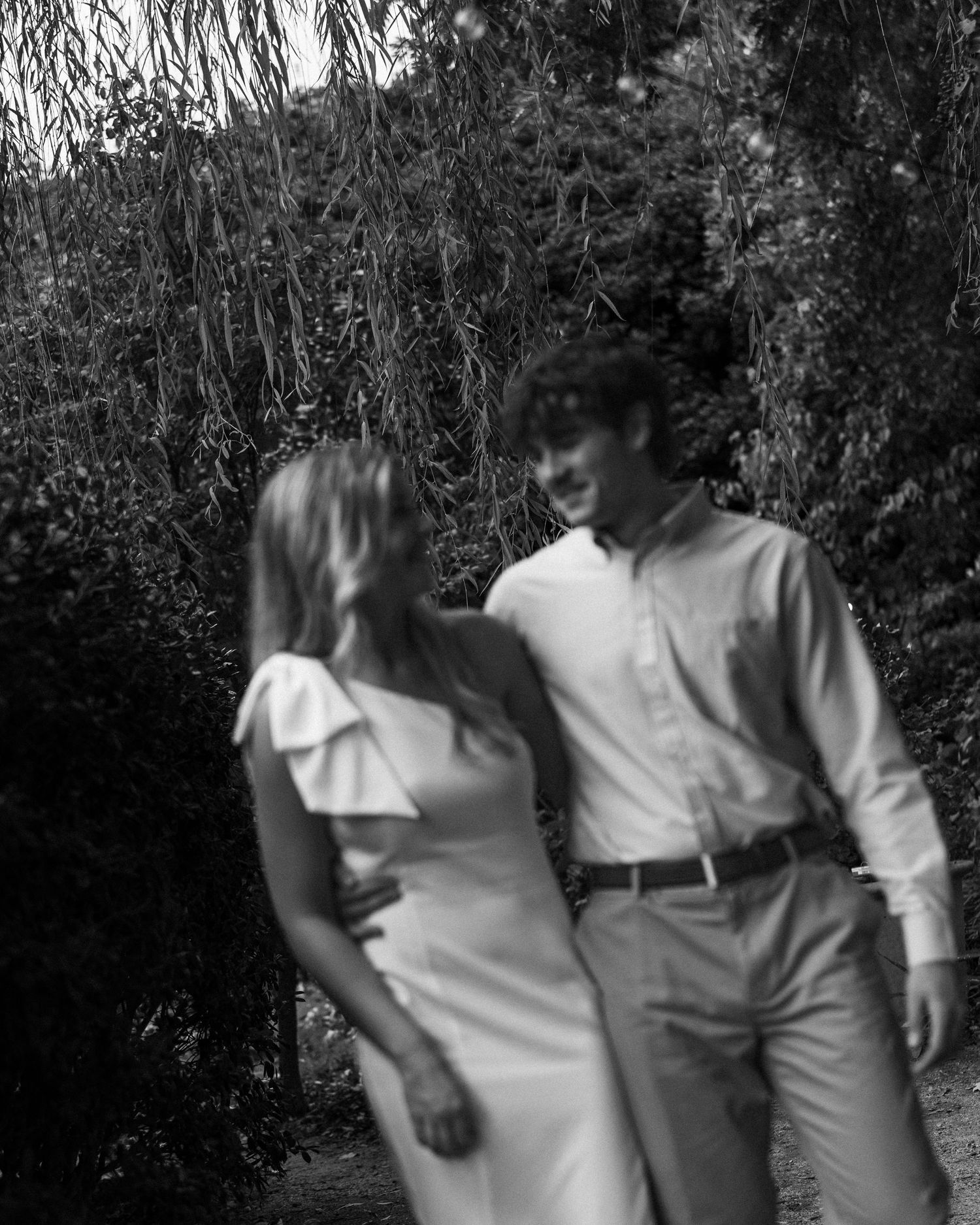 Black and white photo of a couple walking together through a garden path.