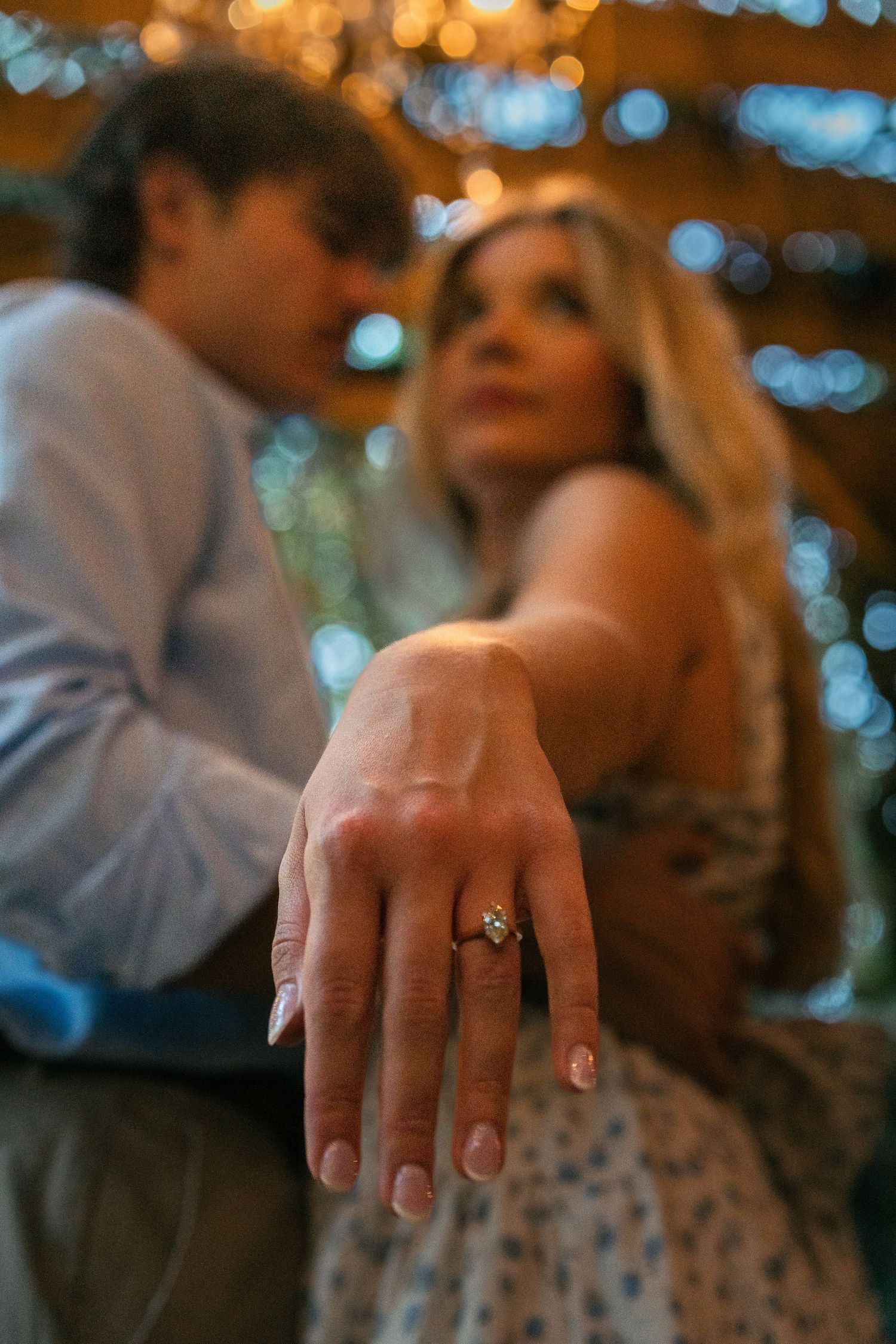 Close-up of newly engaged hand with ring against warm bokeh lighting.