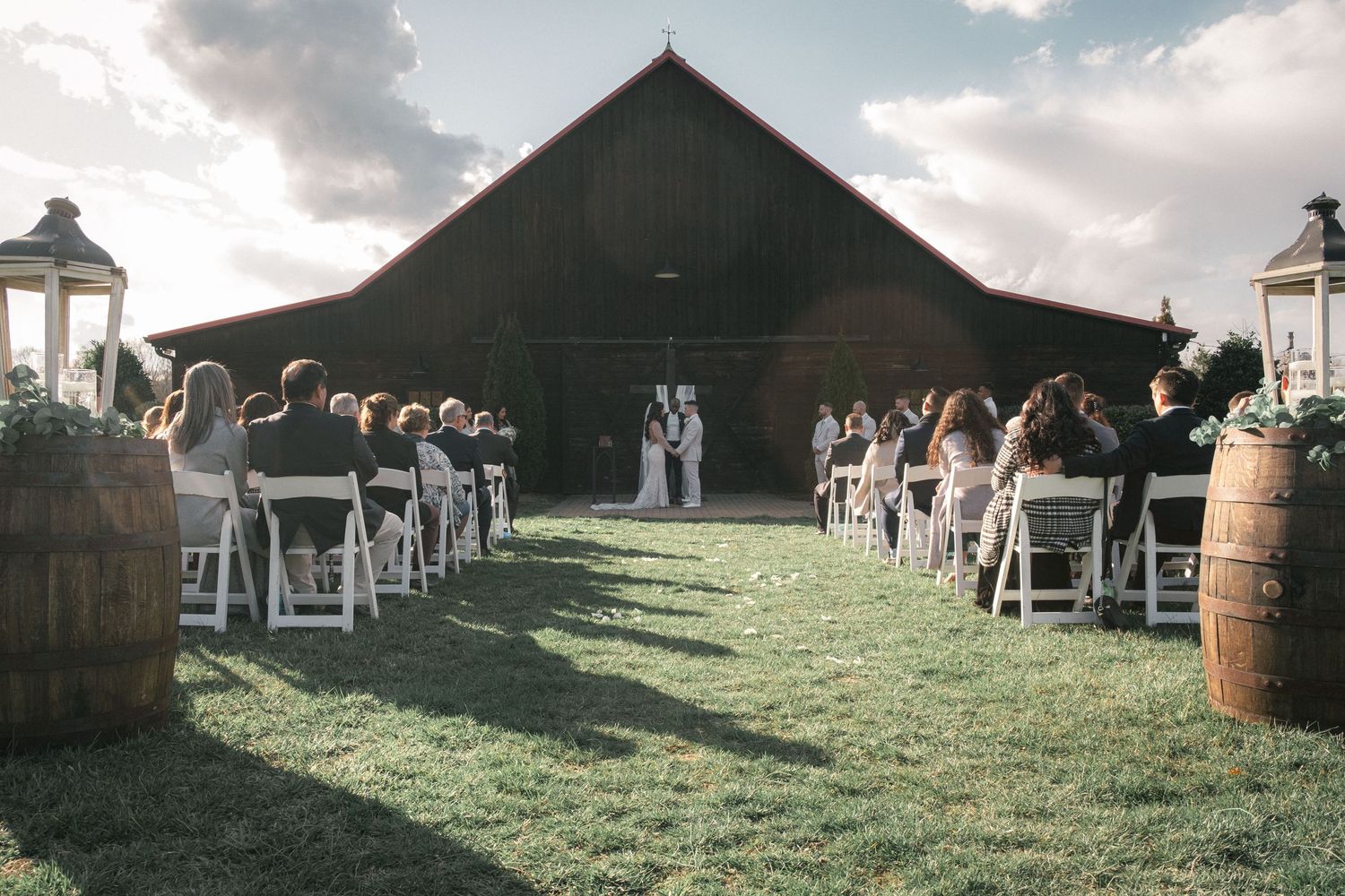 Rustic outdoor wedding venue setup with wooden benches and a barn in the background.