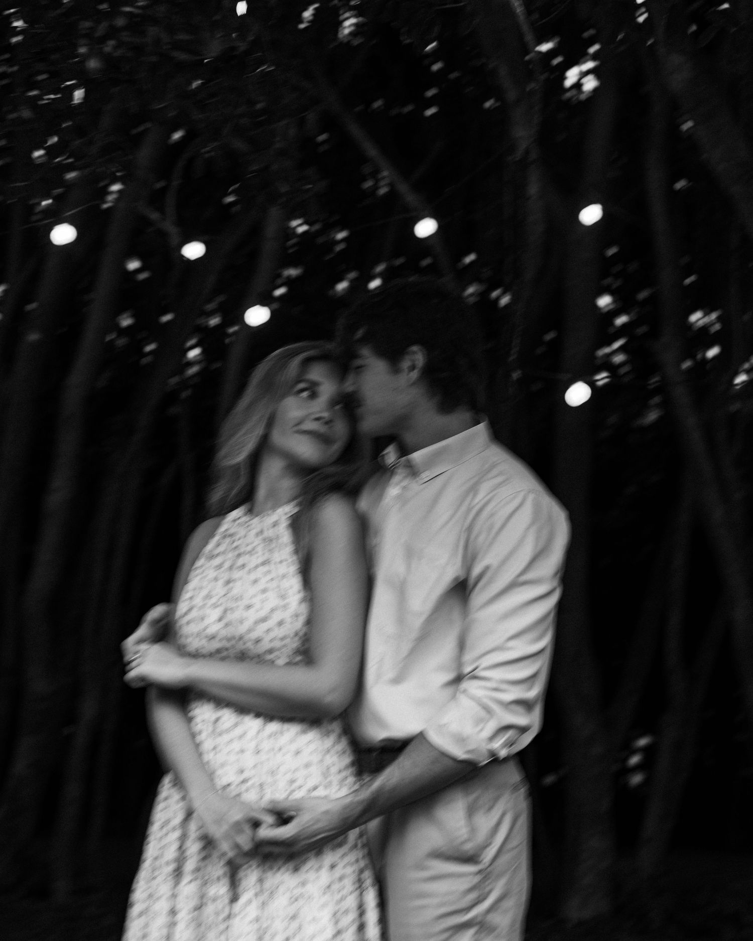 A romantic black and white portrait of a couple embracing under twinkling lights.