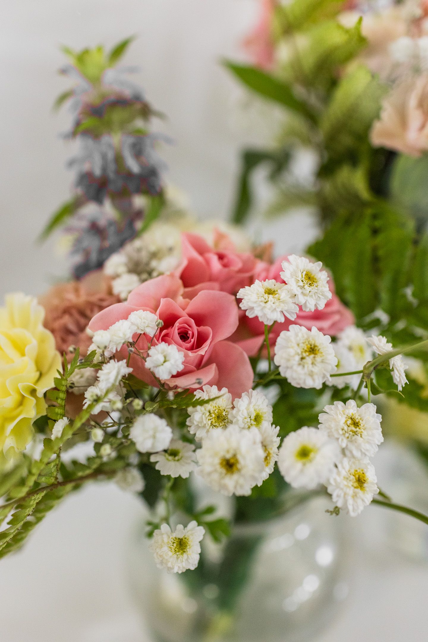 Delicate floral arrangement featuring pink roses, white daisies, and yellow blooms against a light background.