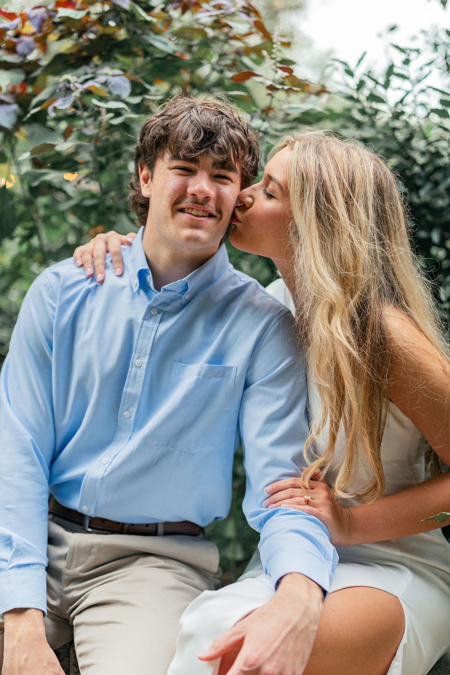 A sweet moment shared between a couple in casual attire against green foliage.