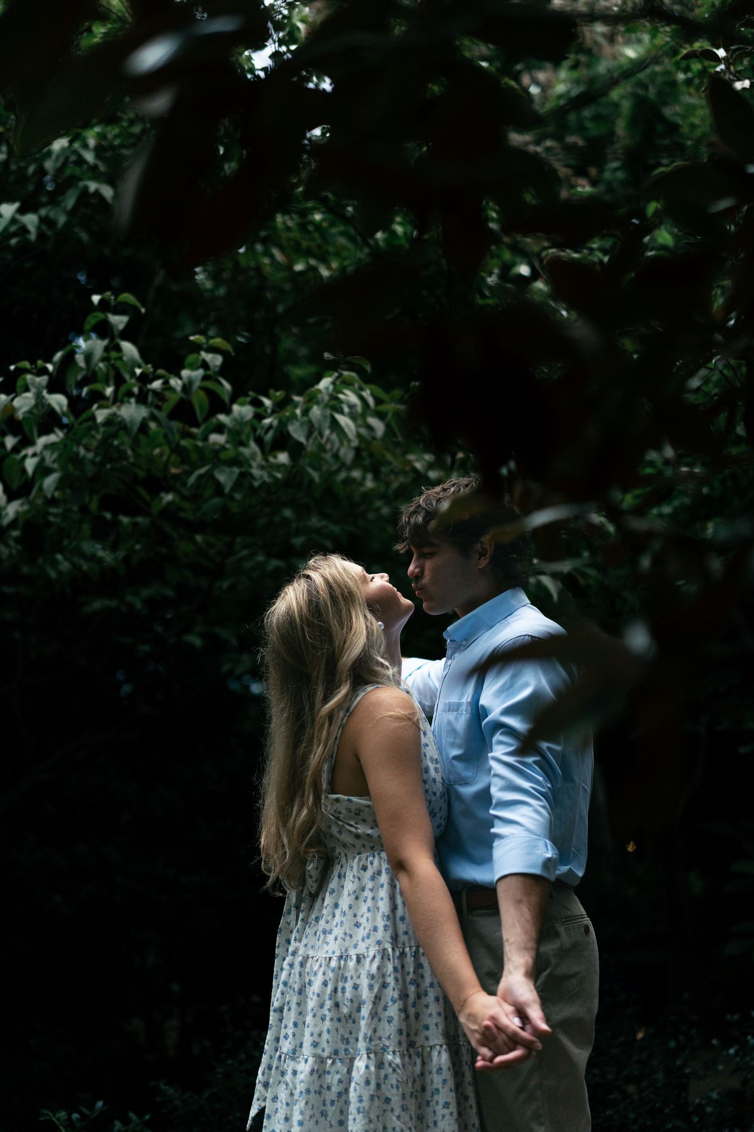 Couple embracing in a garden setting wearing light blue shirt and white patterned dress.