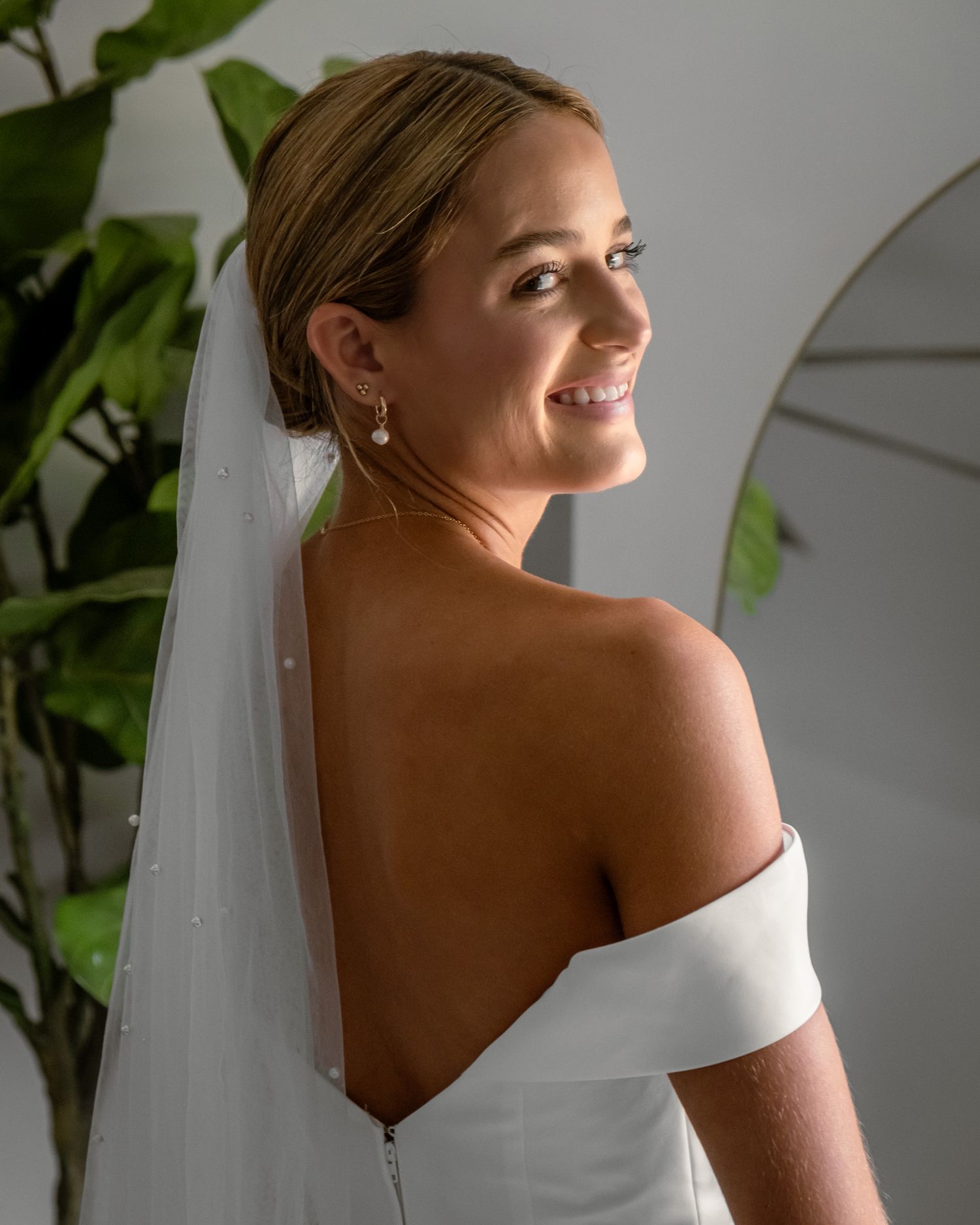 Elegant off-shoulder wedding dress with flowing veil captured in natural light.