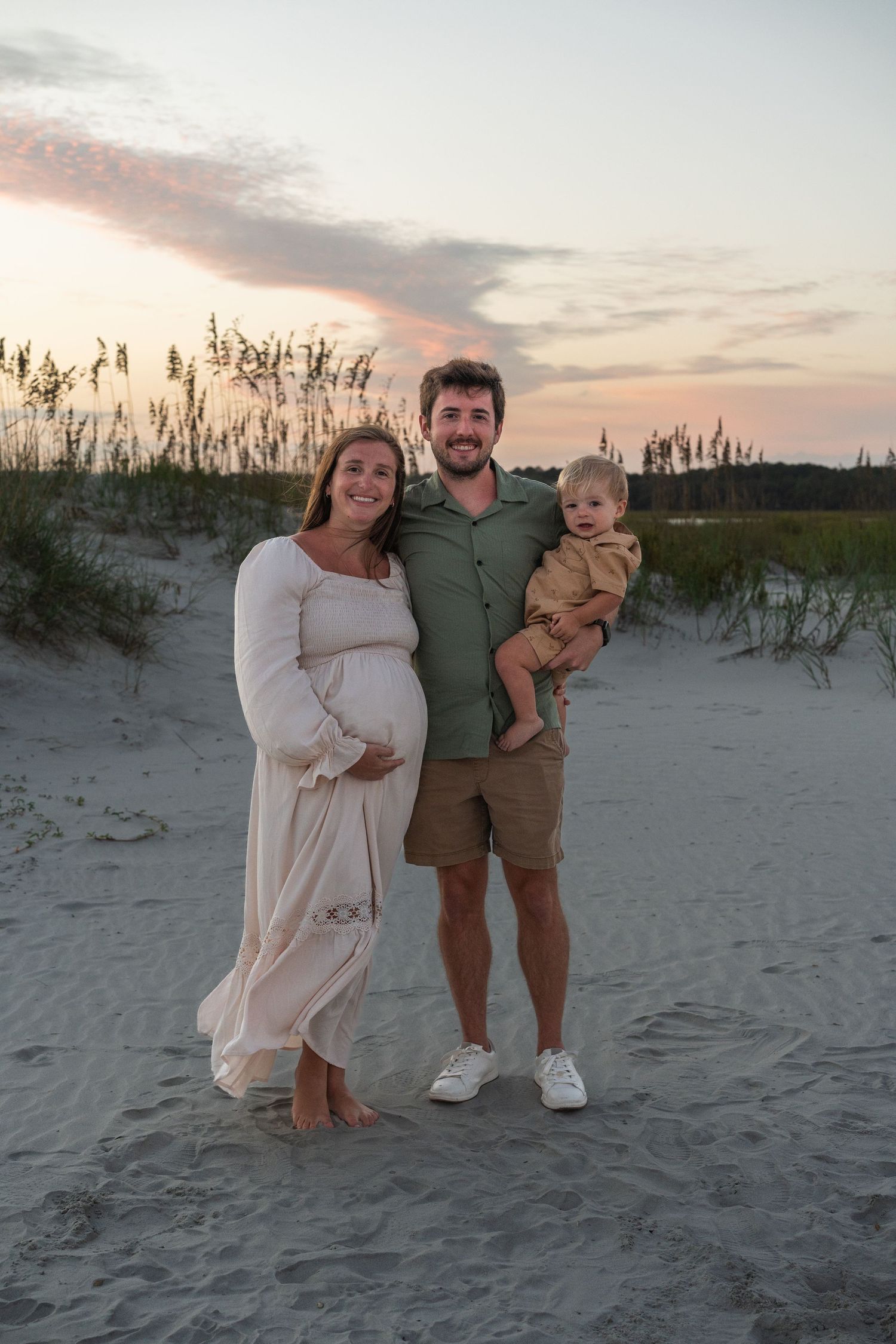 Family portrait on a beach with sand dunes and sea oats at sunset.