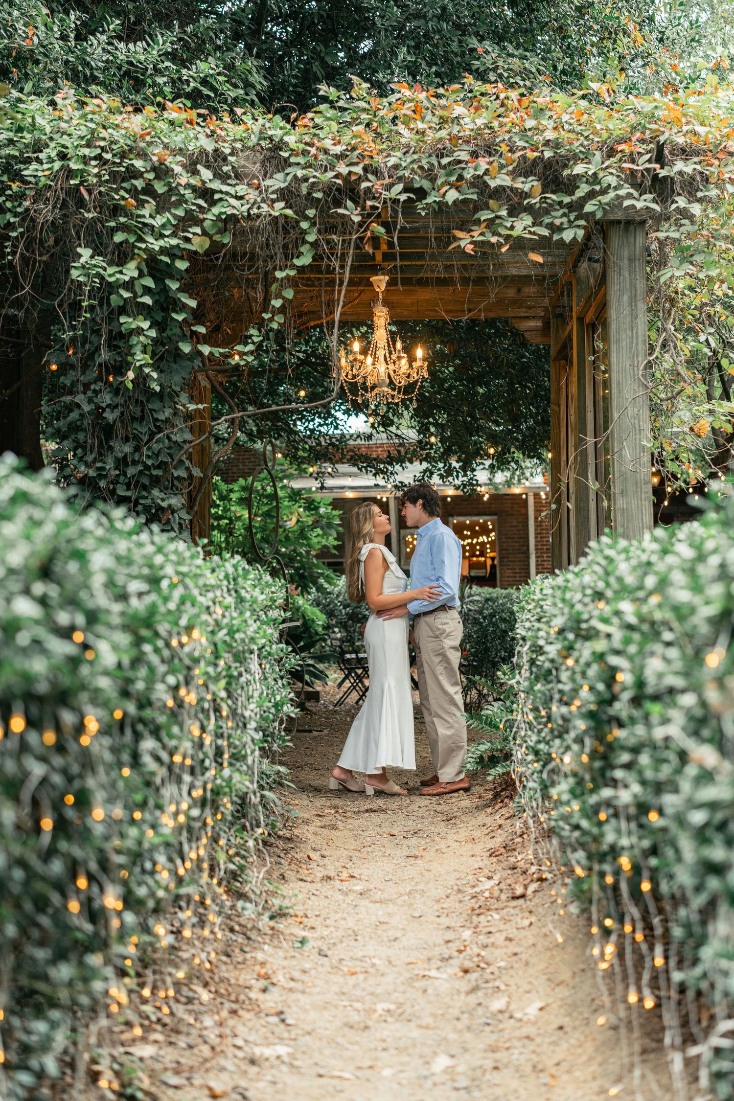 Garden pathway lined with greenery and string lights creating a romantic ambiance.