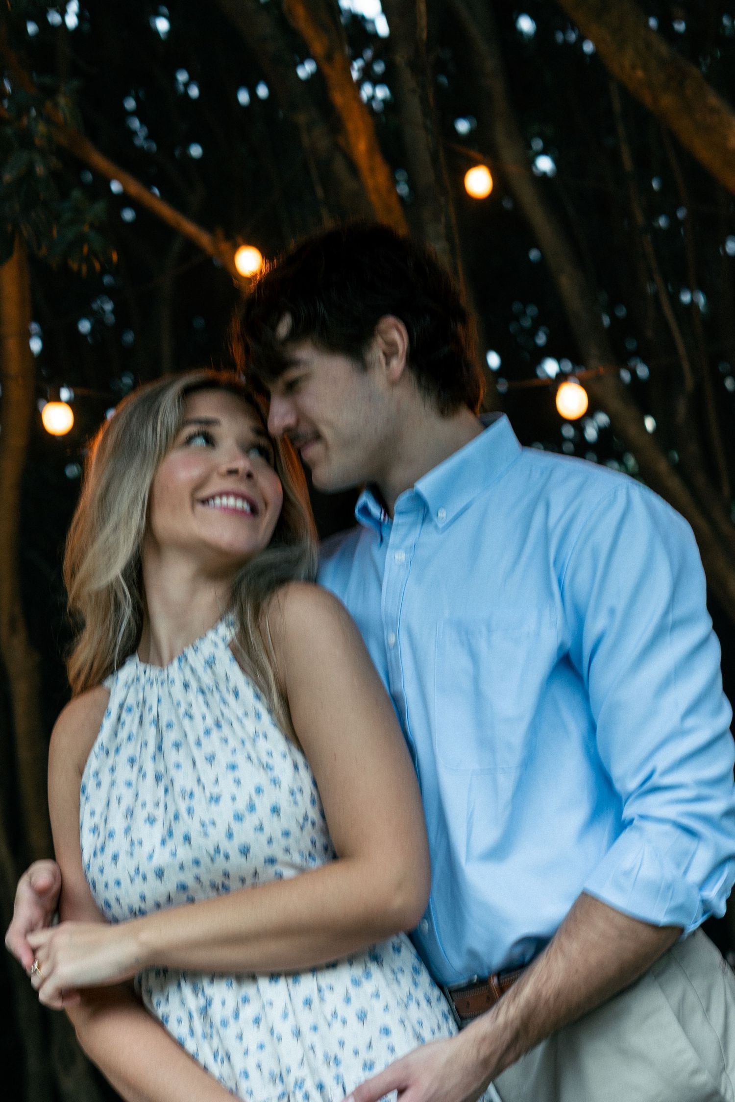Joyful couple laughing together under twinkling outdoor lights.
