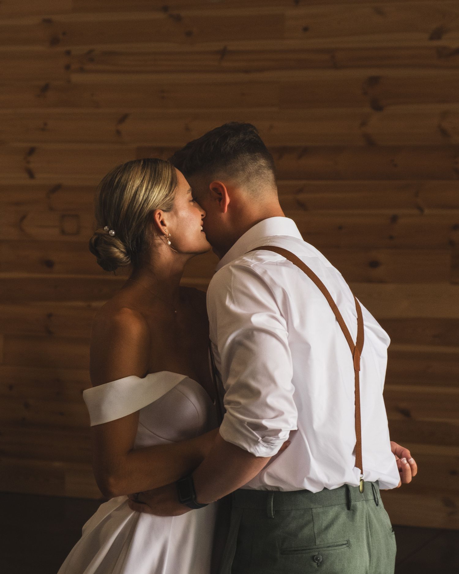 Intimate dance moment between newlyweds against wooden wall background.