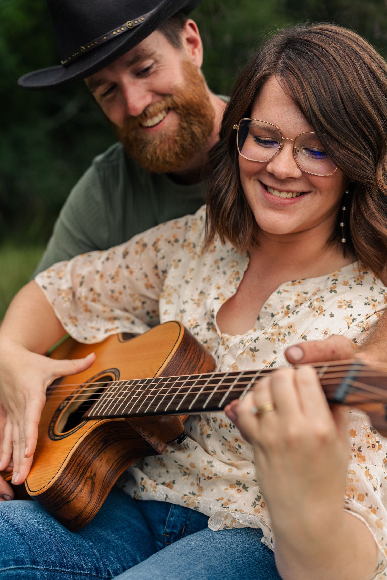 A couple shares a joyful moment while playing acoustic guitar outdoors.