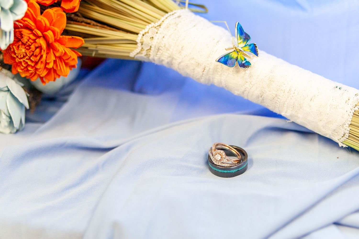 Beautiful wedding details featuring a bouquet with a butterfly on the stems and wedding rings, thoughtfully arranged to capture the couple.