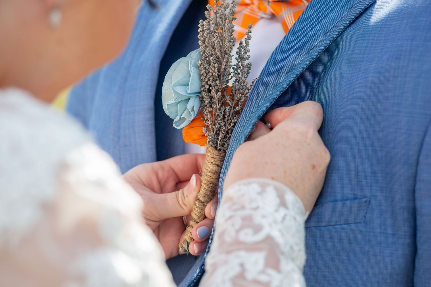 Bride delicately pinning the boutonnière onto the groom’s suit, capturing a heartfelt and intimate moment during a perfectly planned wedding