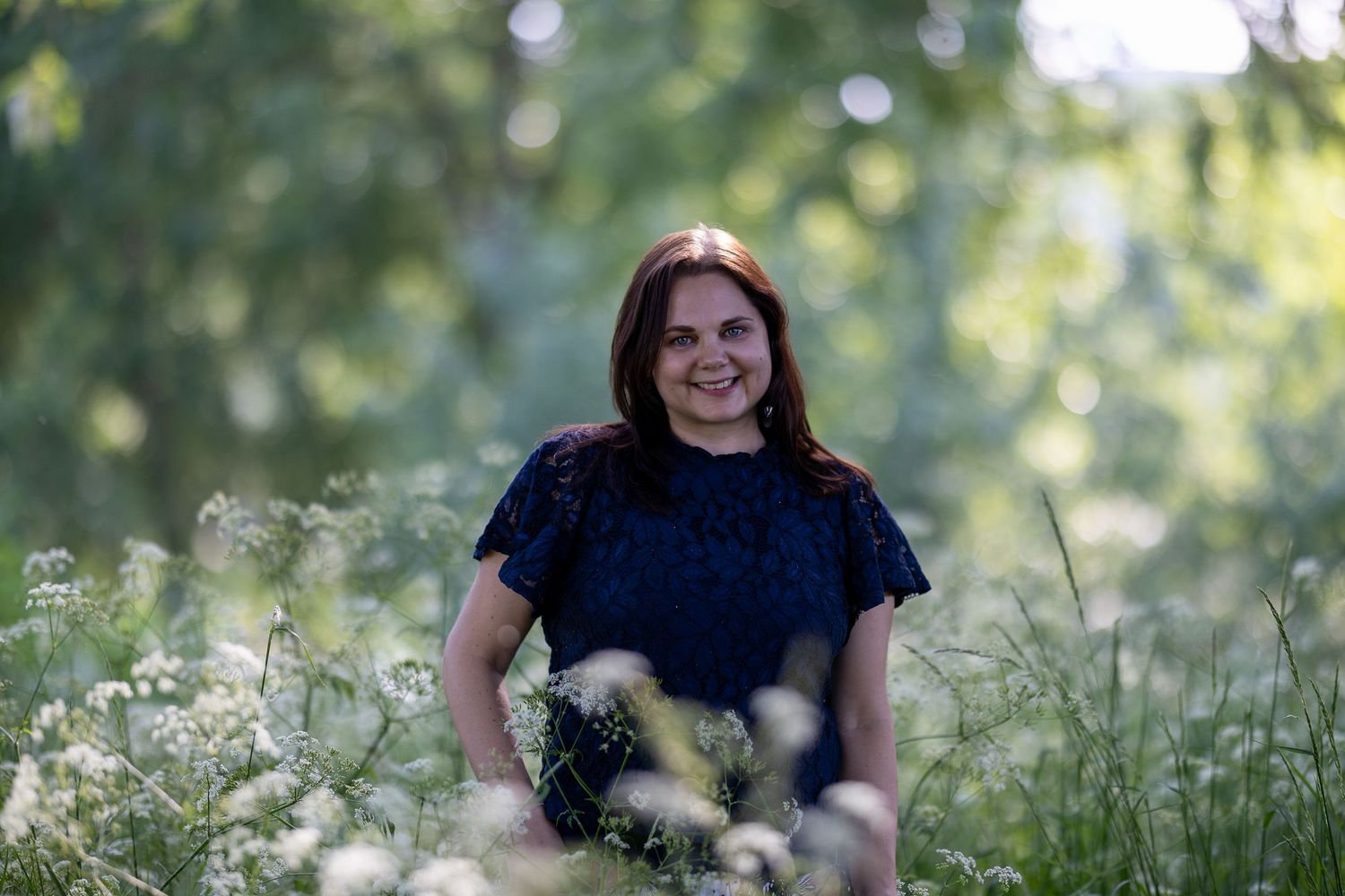 Colour portrait of a woman in a dark blue top, standing in a wildflower meadow, smiling
