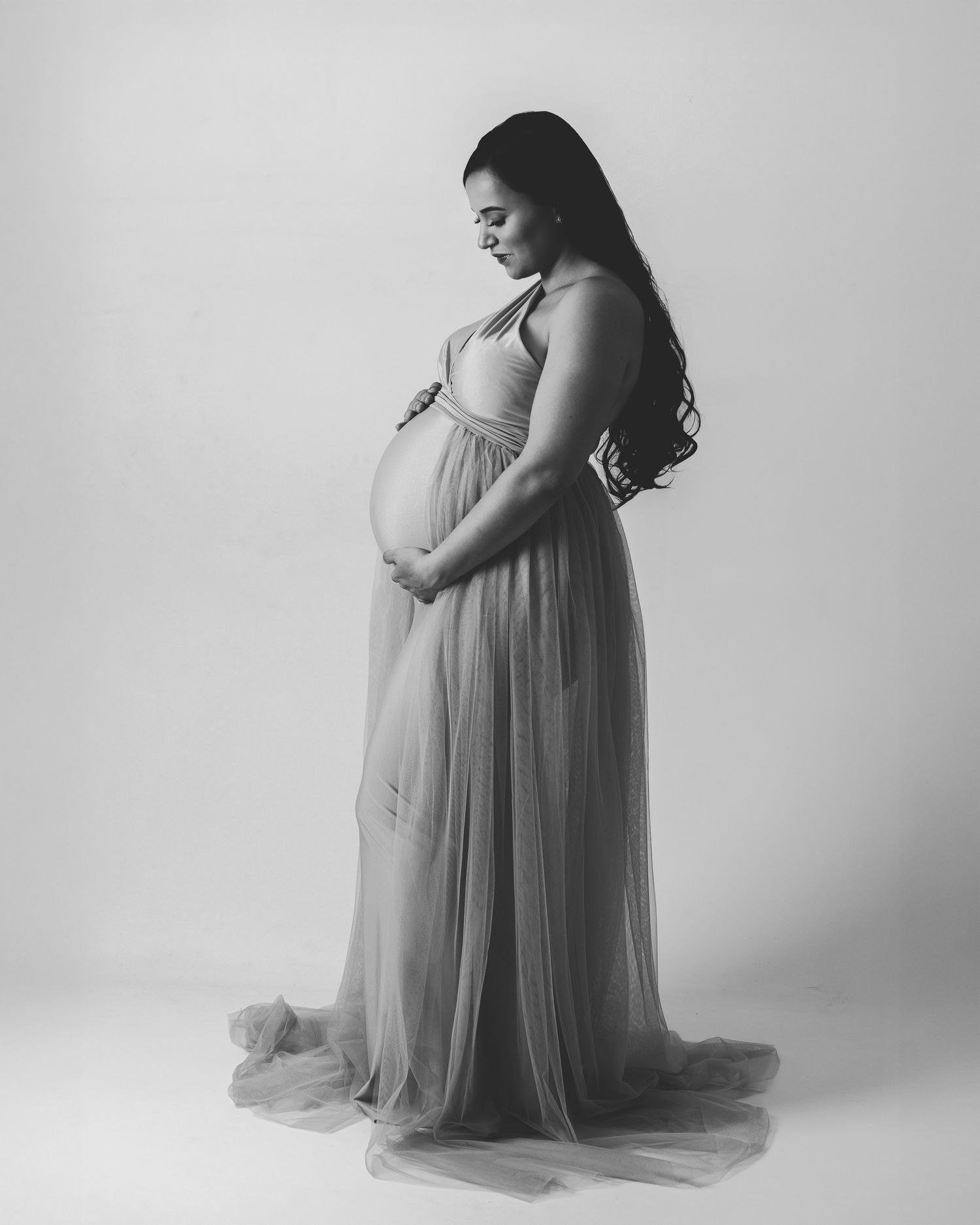 Black and white portrait of a woman in a long flowing sheer gown, soft studio background, gentle side profile