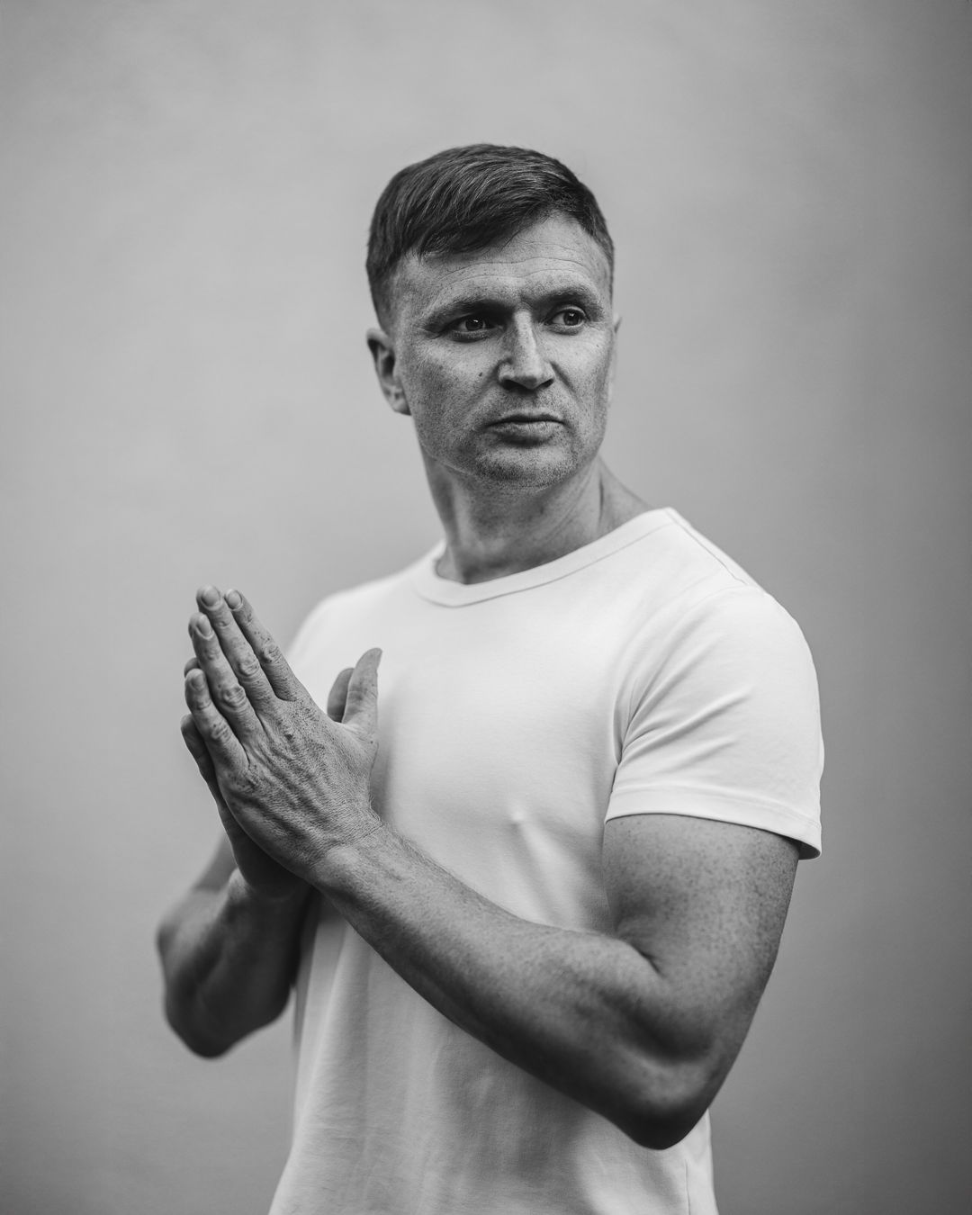 Black and white portrait of a man in a white t-shirt, hands pressed together, against a plain background