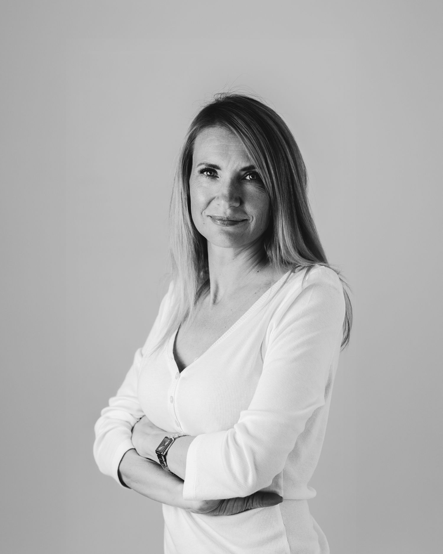 Black and white portrait of a woman in a white long-sleeve top, arms crossed, light grey background