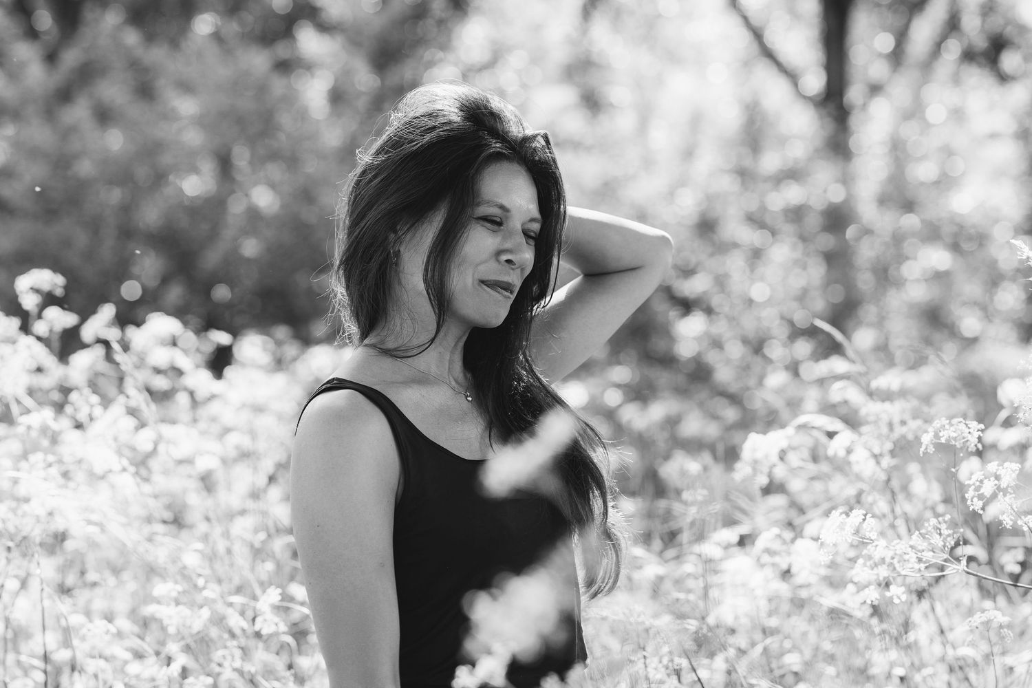 Black and white portrait of a woman in a wildflower meadow, hand to her head, artistic outdoor pose