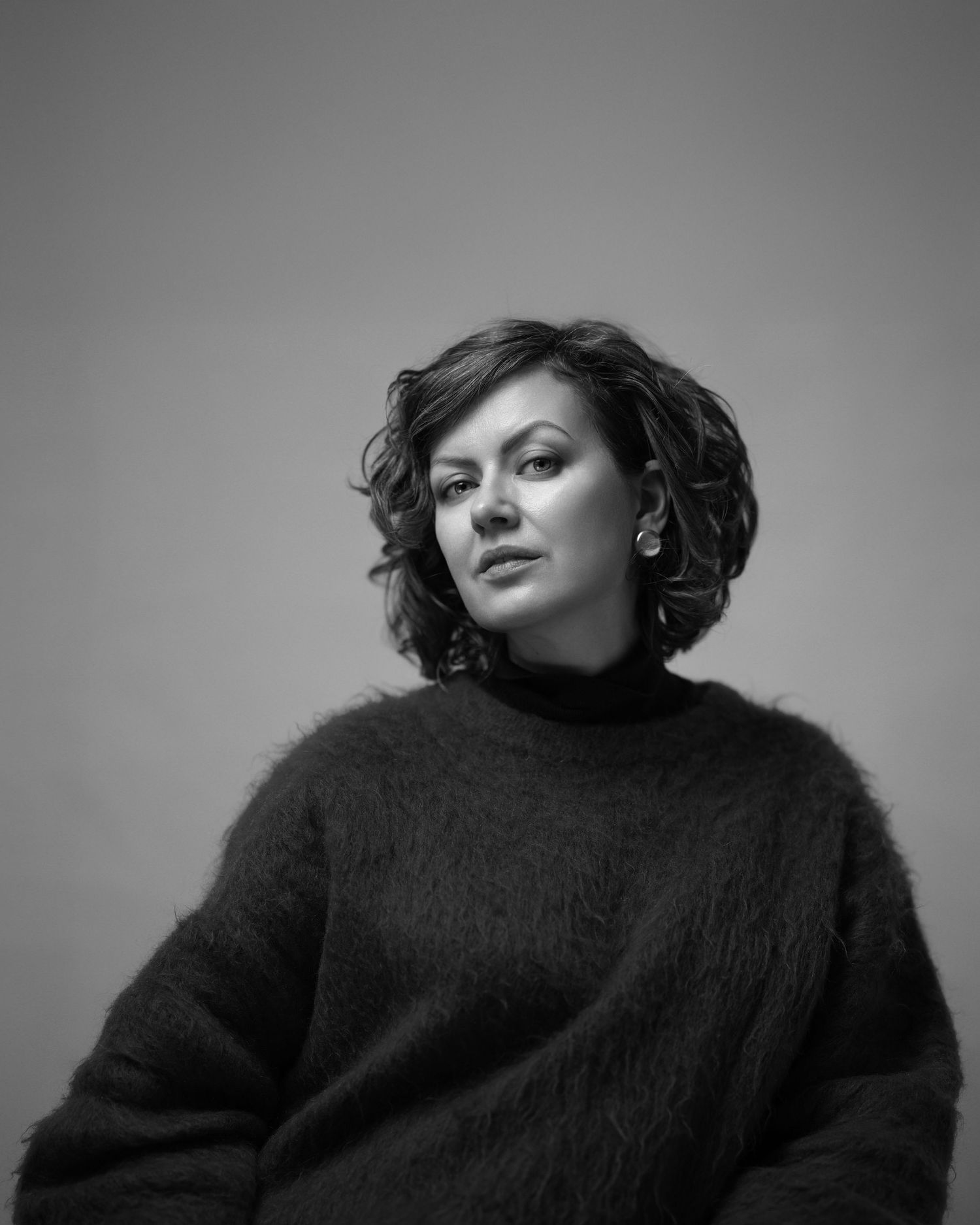 Black and white portrait of a woman with short dark wavy hair in a dark roll-neck, soft studio light