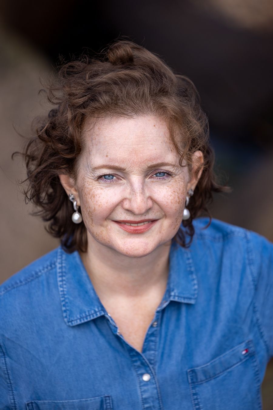 Colour headshot of a woman with curly hair in a bright blue shirt, smiling warmly