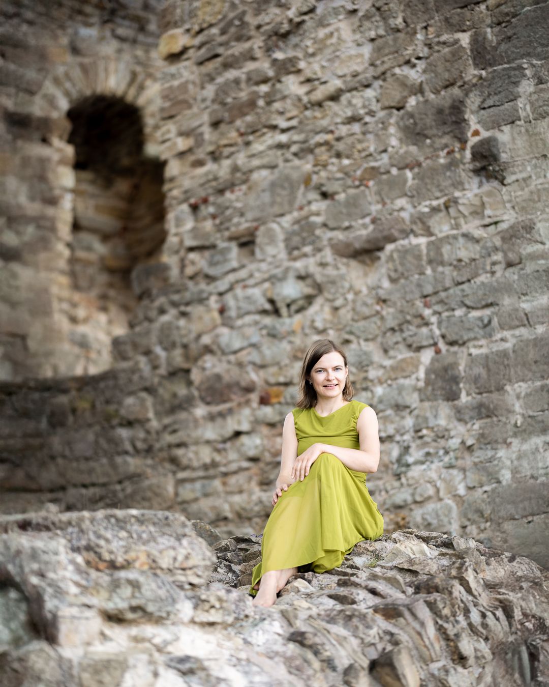 Colour portrait of a woman in a yellow-green dress seated among ancient stone castle ruins