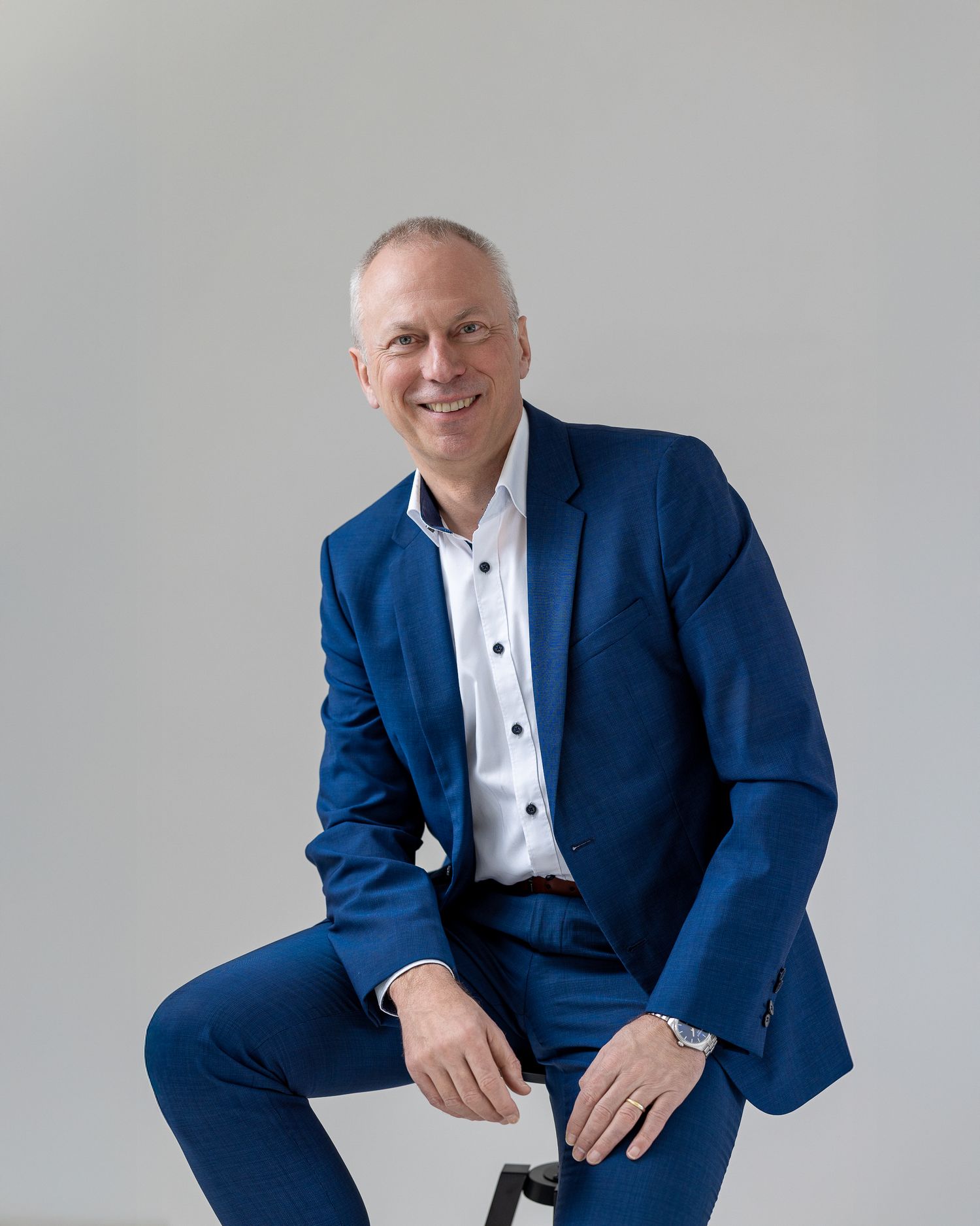 Colour headshot of a man in a bright blue suit, seated, against a light grey background