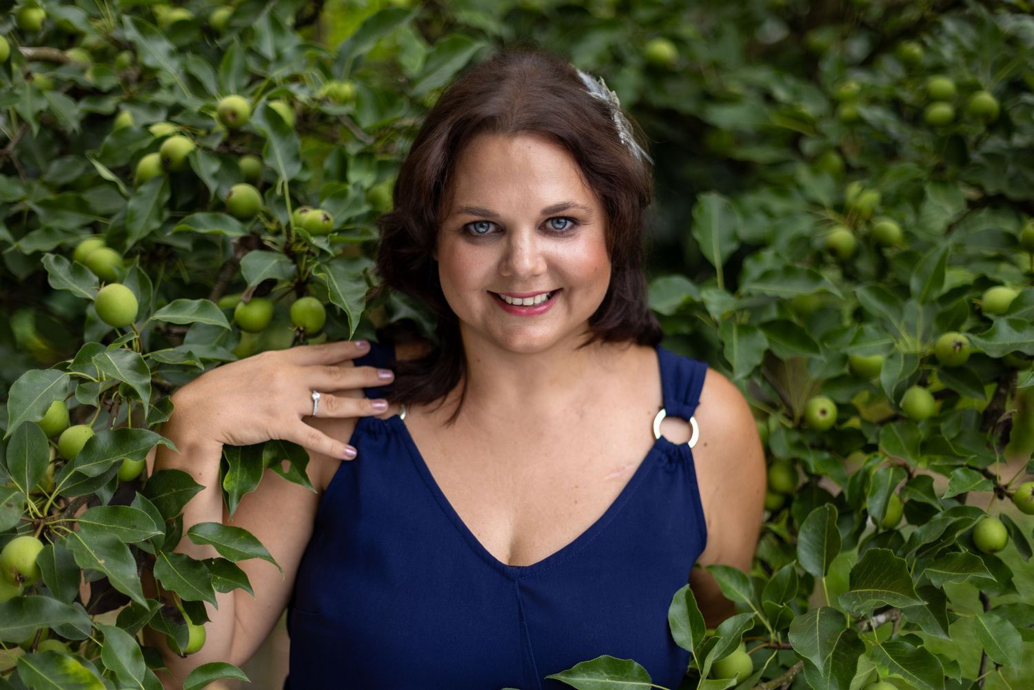 Colour portrait of a woman in a navy top smiling among green foliage