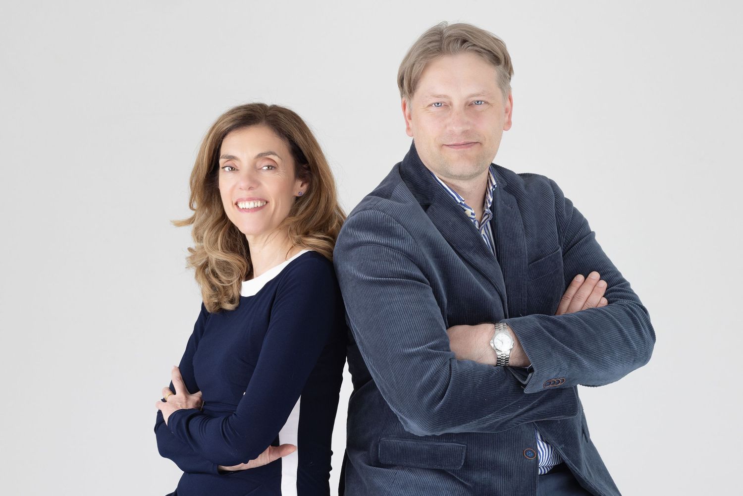 Colour team portrait of a woman and man standing back-to-back in dark professional clothing, light grey background