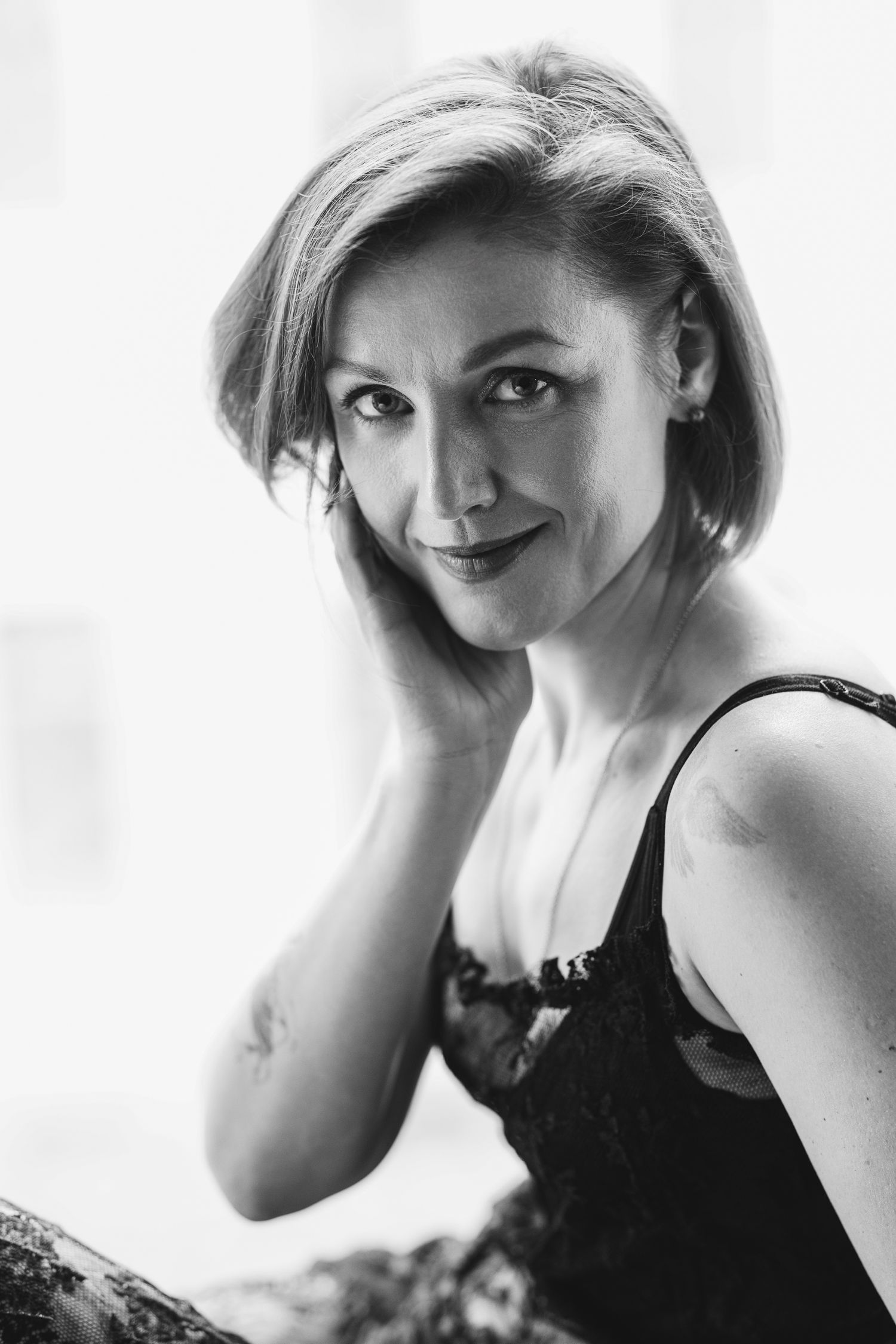 Black and white boudoir portrait of a woman with short blonde hair, hand near her face, soft natural light