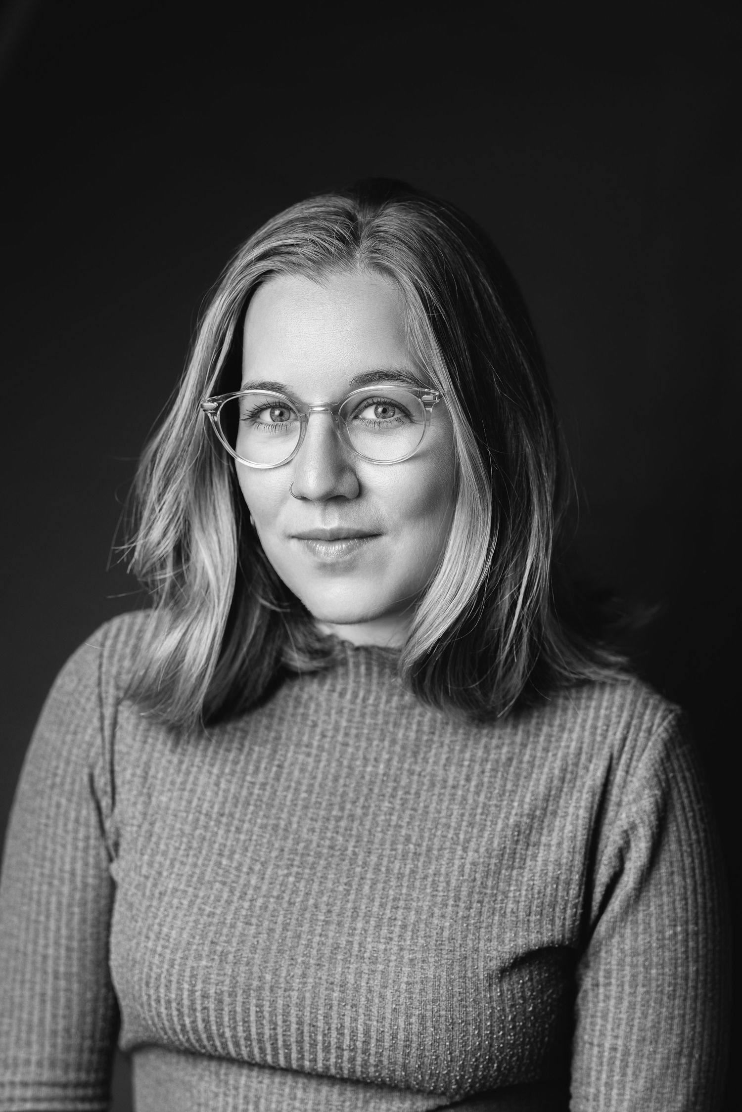 Black and white portrait of a woman with straight hair and glasses in a ribbed top against a dark background