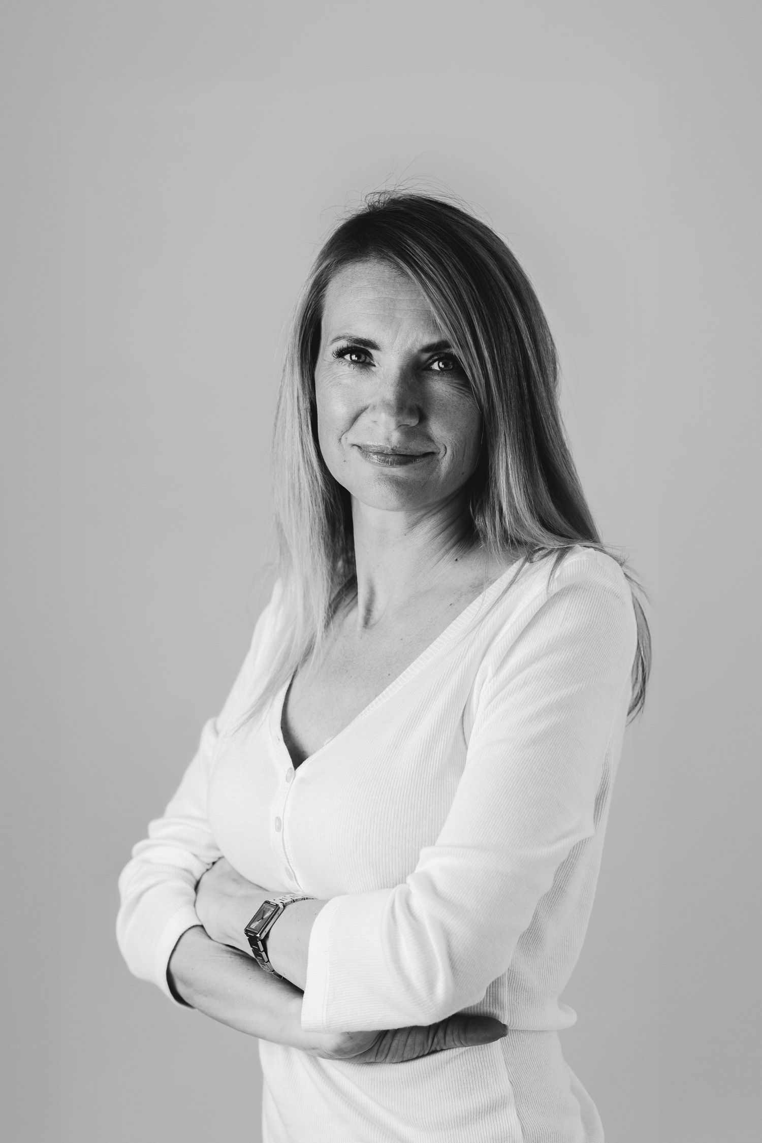 Black and white business portrait of a woman with light hair and white top, arms crossed, Brussels
