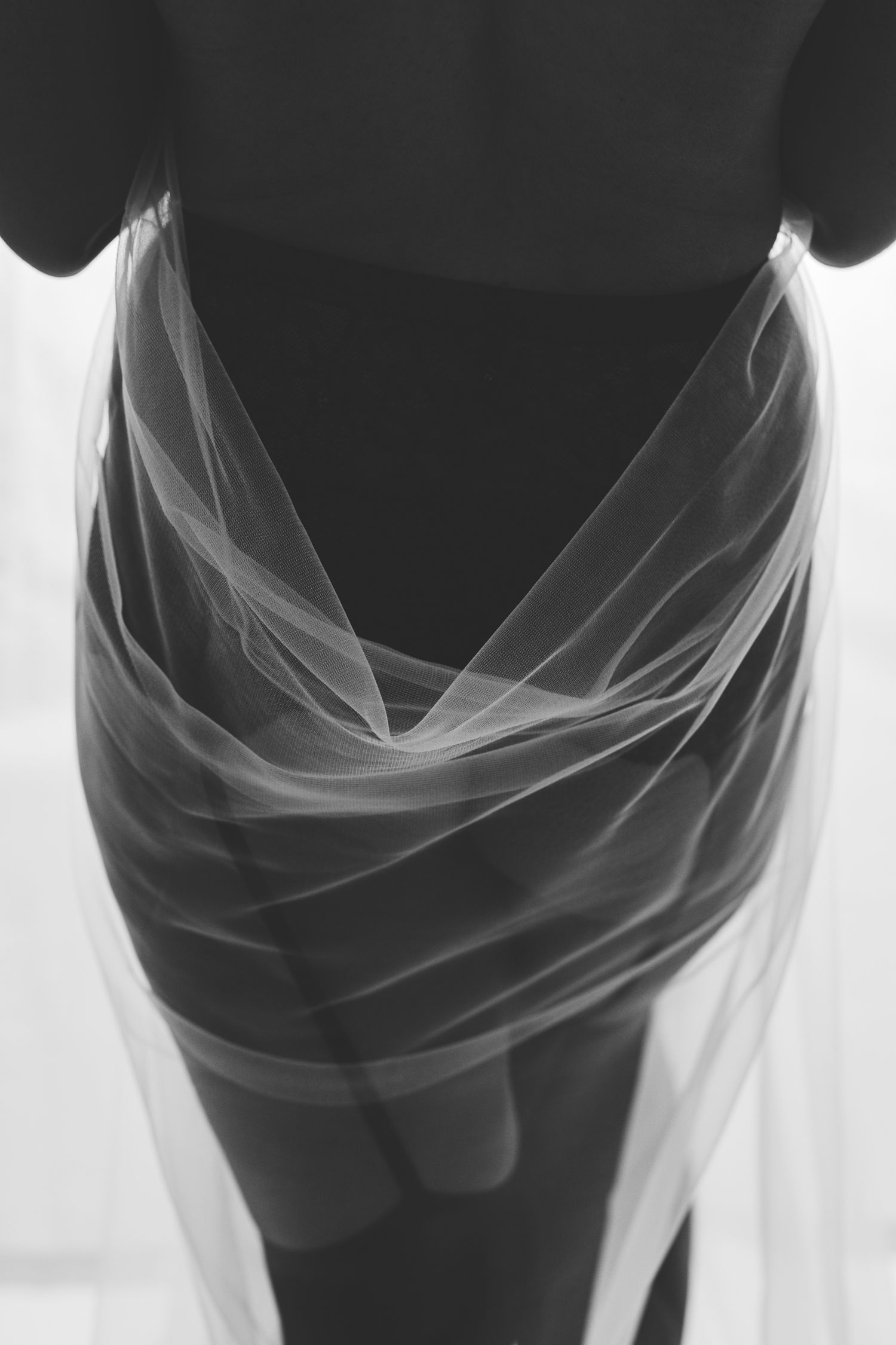 Black and white boudoir detail of sheer translucent fabric draped around a figure, abstract composition, high-key light