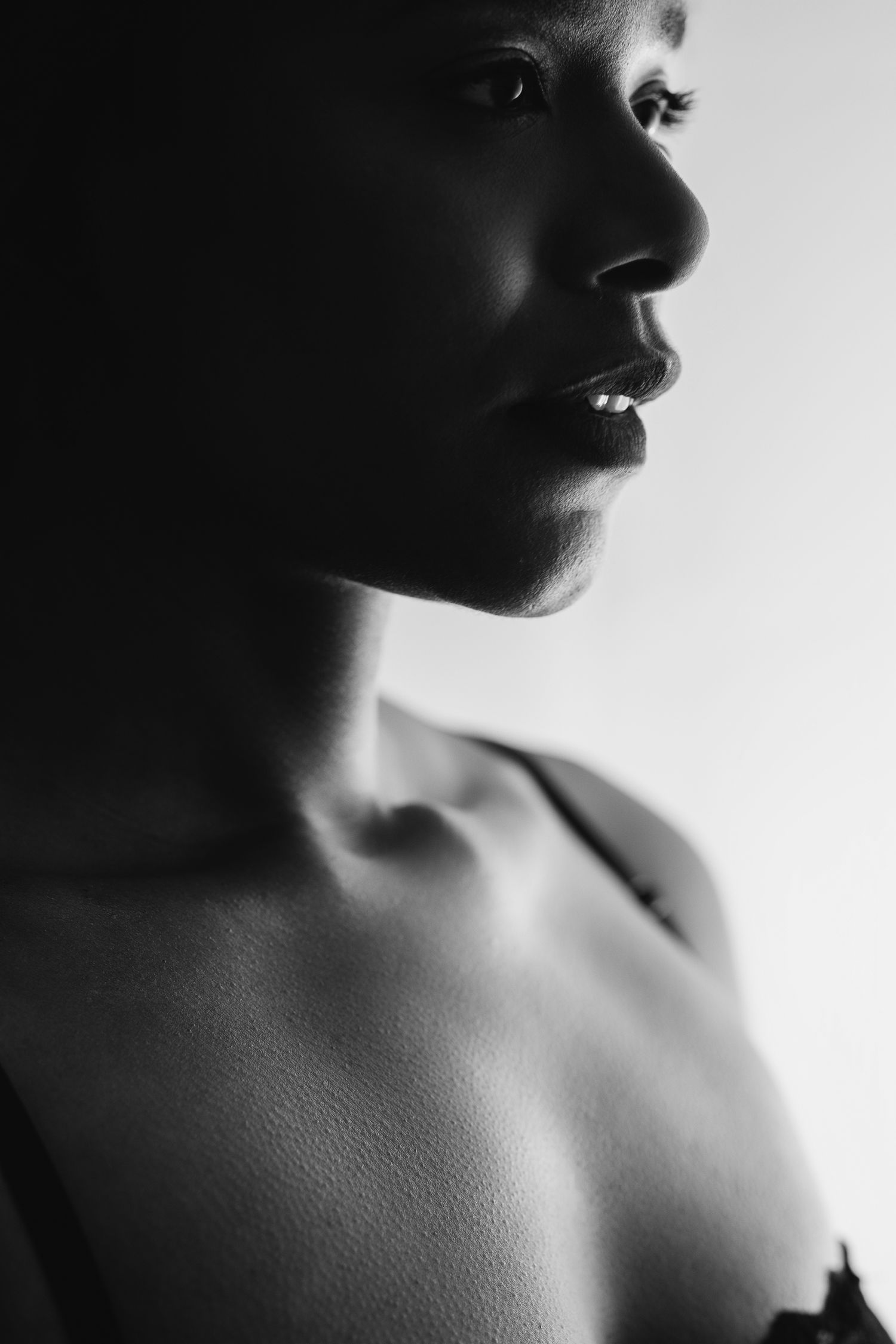Black and white boudoir portrait, close crop of a woman's face and bare shoulder in profile, soft high-key light