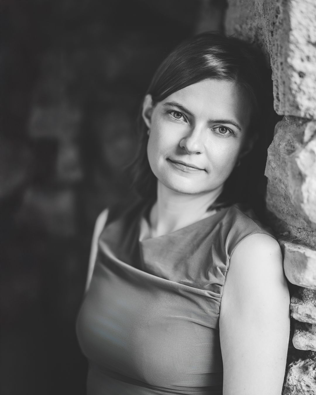 Black and white portrait of a woman with dark hair, smiling, against a stone wall