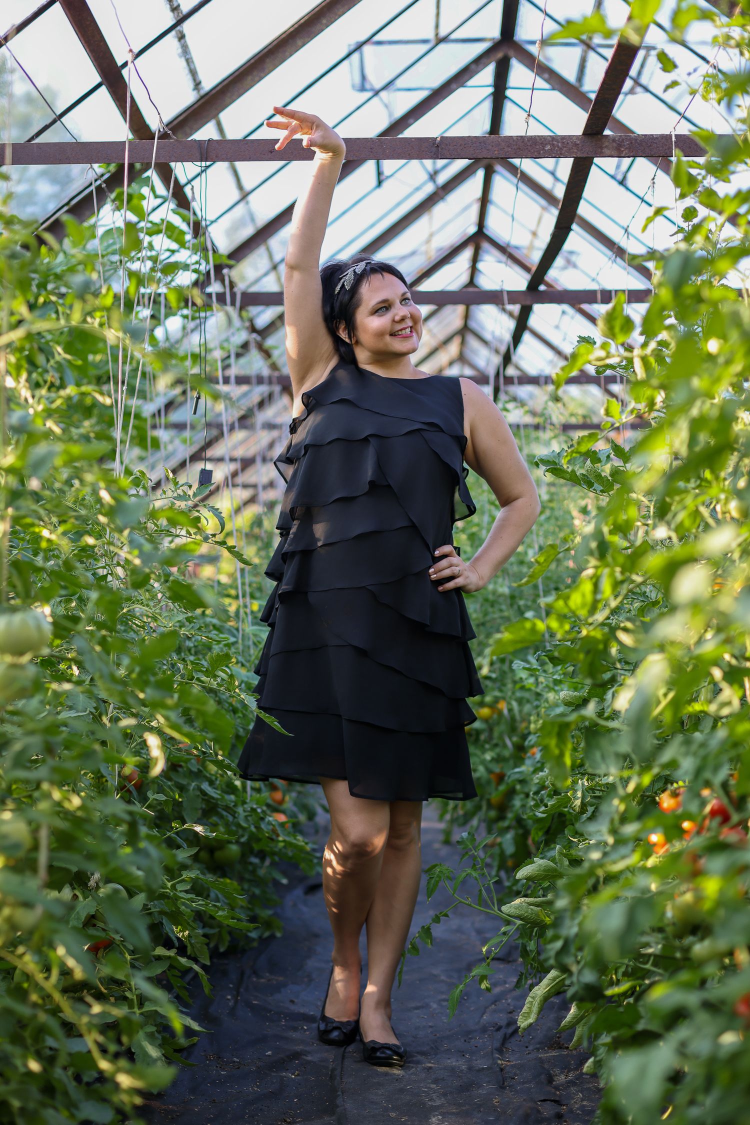 Black and white portrait of a woman outdoors under trailing foliage, smiling, hands clasped near her face