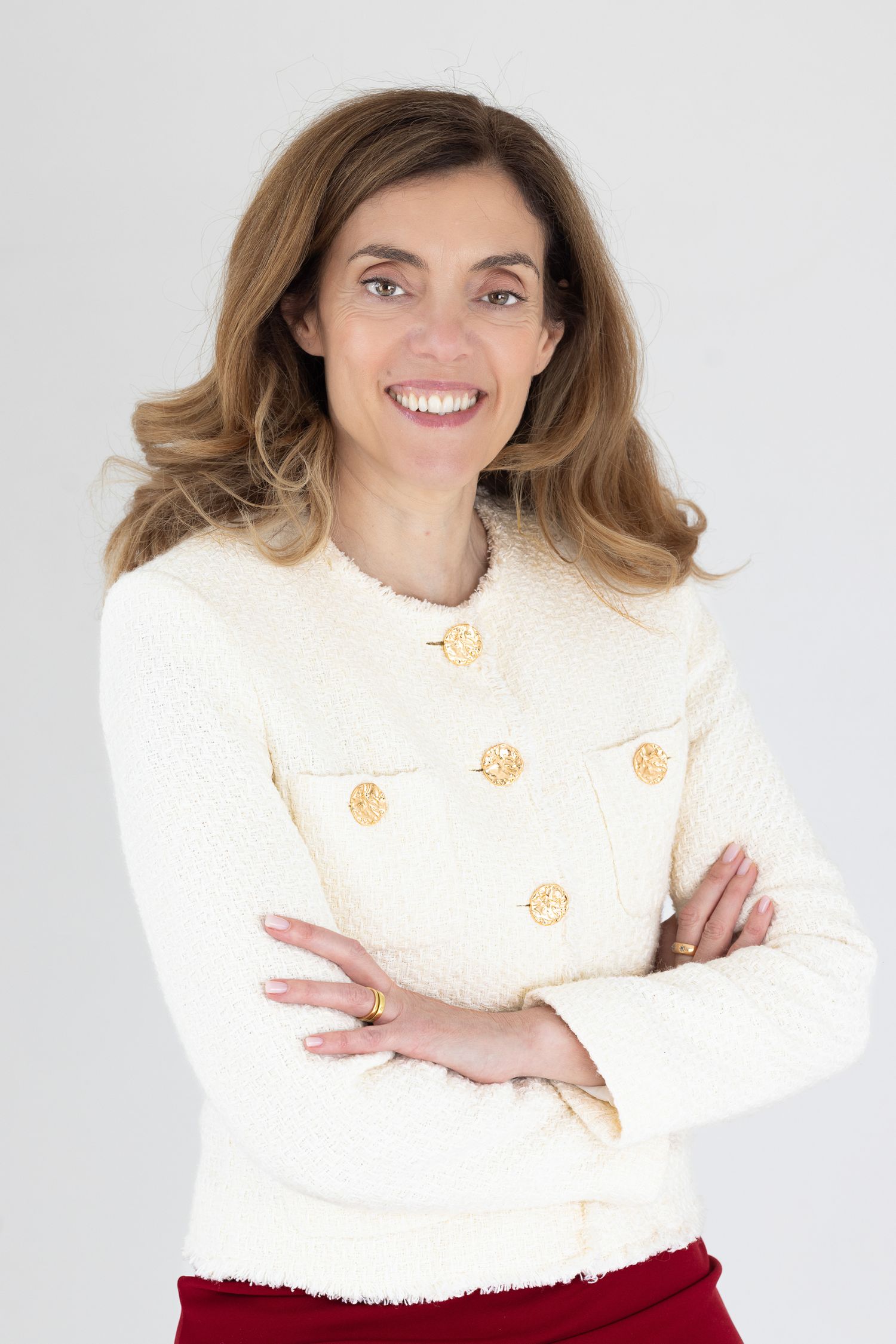Professional headshot of a woman in a cream cardigan with gold buttons, arms crossed, plain grey background