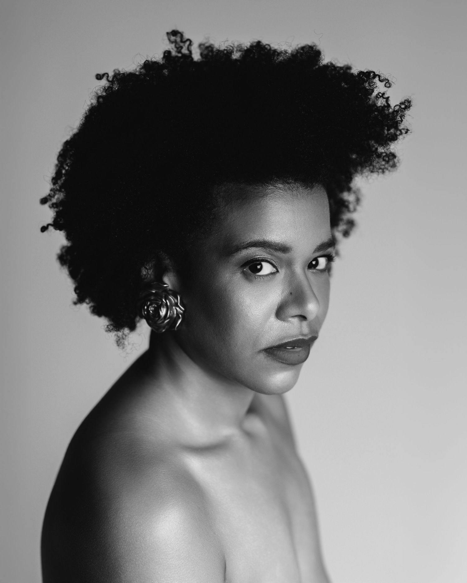 Black and white boudoir portrait of a woman with natural hair, bare shoulders, looking back over her shoulder in soft studio light