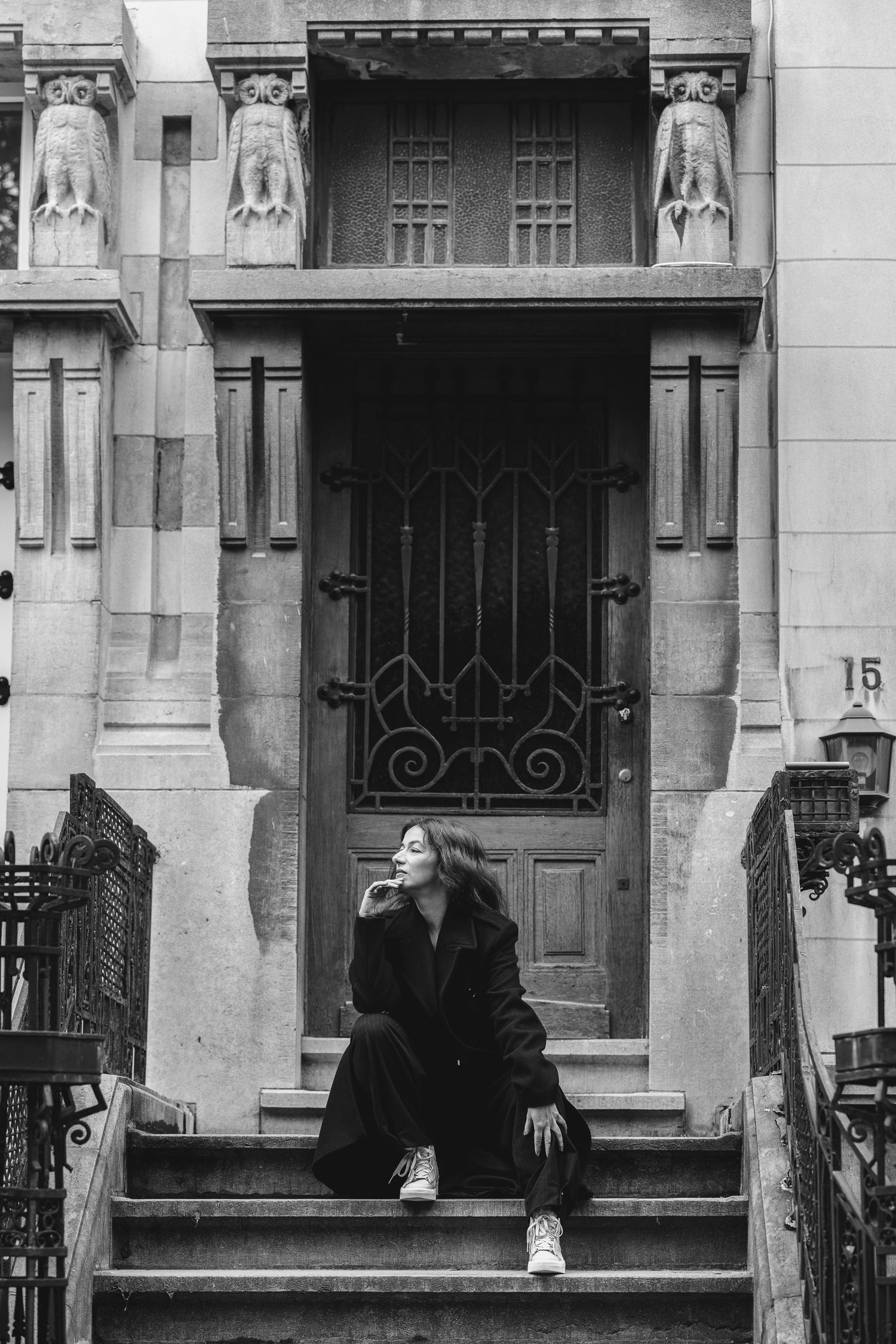 Black and white portrait of a woman seated on the steps of an ornate Art Nouveau doorway