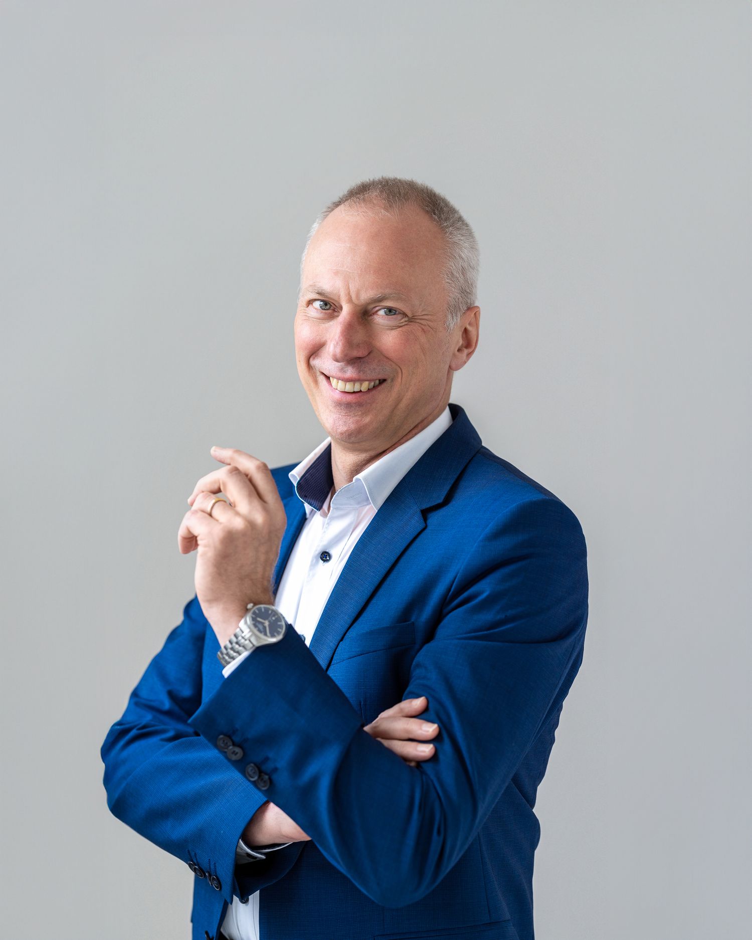 Professional headshot of a man in a bright blue suit jacket, smiling, light grey background