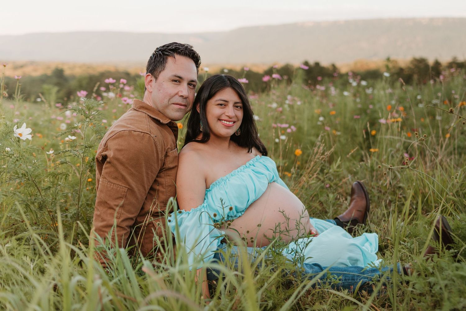 Couple sitting and looking at camera in a wildflower field at Fox Mountain Farms, Chattanooga, TN – maternity session, soft summer light