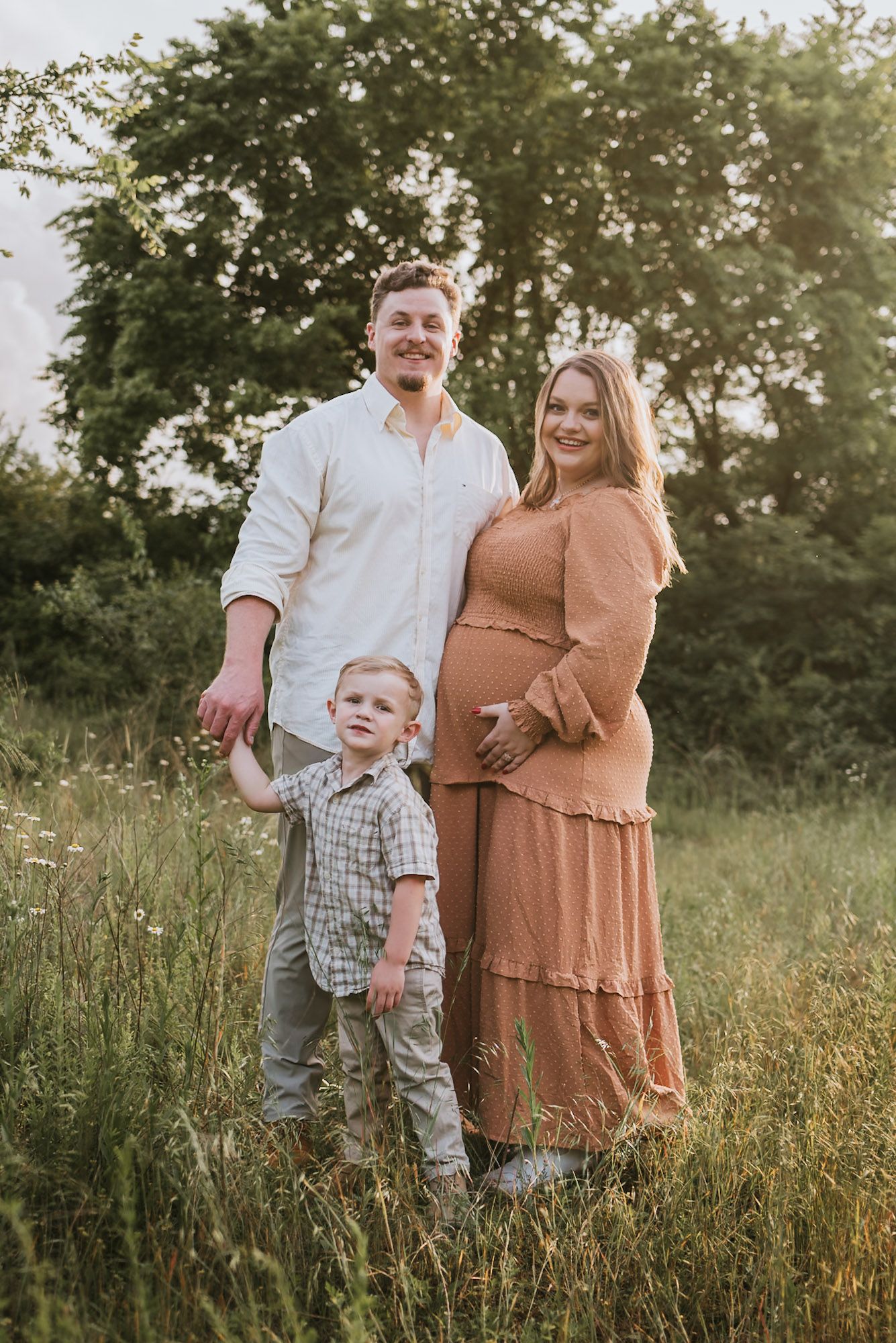 Expecting couple standing close with toddler in front smiling at camera in field, family maternity session raccoon mountain Chattanooga TN