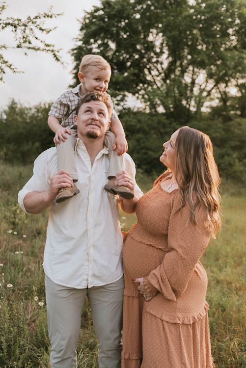 Expecting couple in a sunlit field with their toddler on dads shoulders during an outdoor family maternity session at raccoon mountain, TN