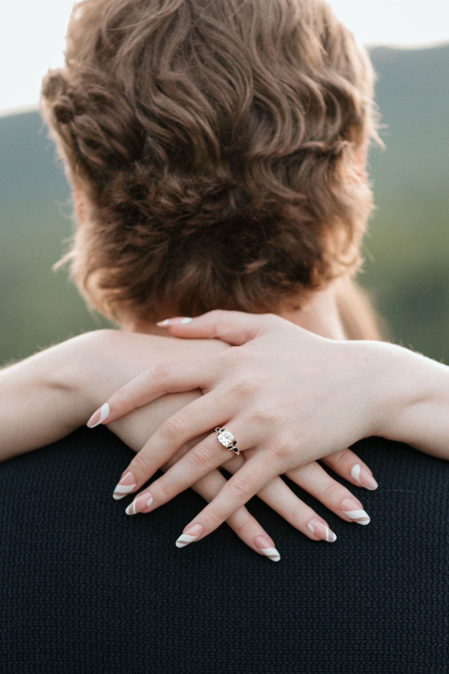 Close up of woman's hands wrapped around boyfriends neck during surprise proposal session, close up of engagement ring