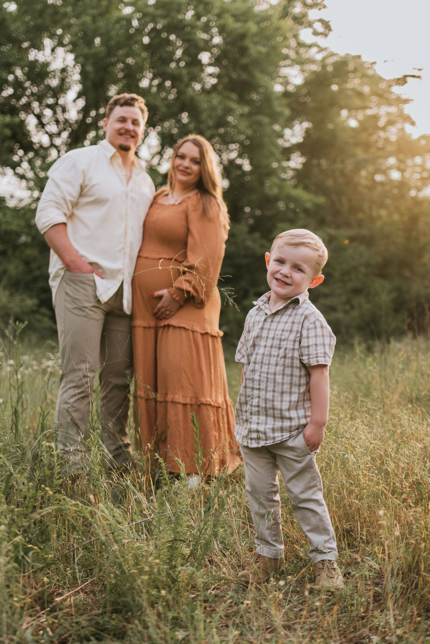 Toddler looking at camera with parents in background in a field in Chattanooga, TN – family maternity session, soft summer light