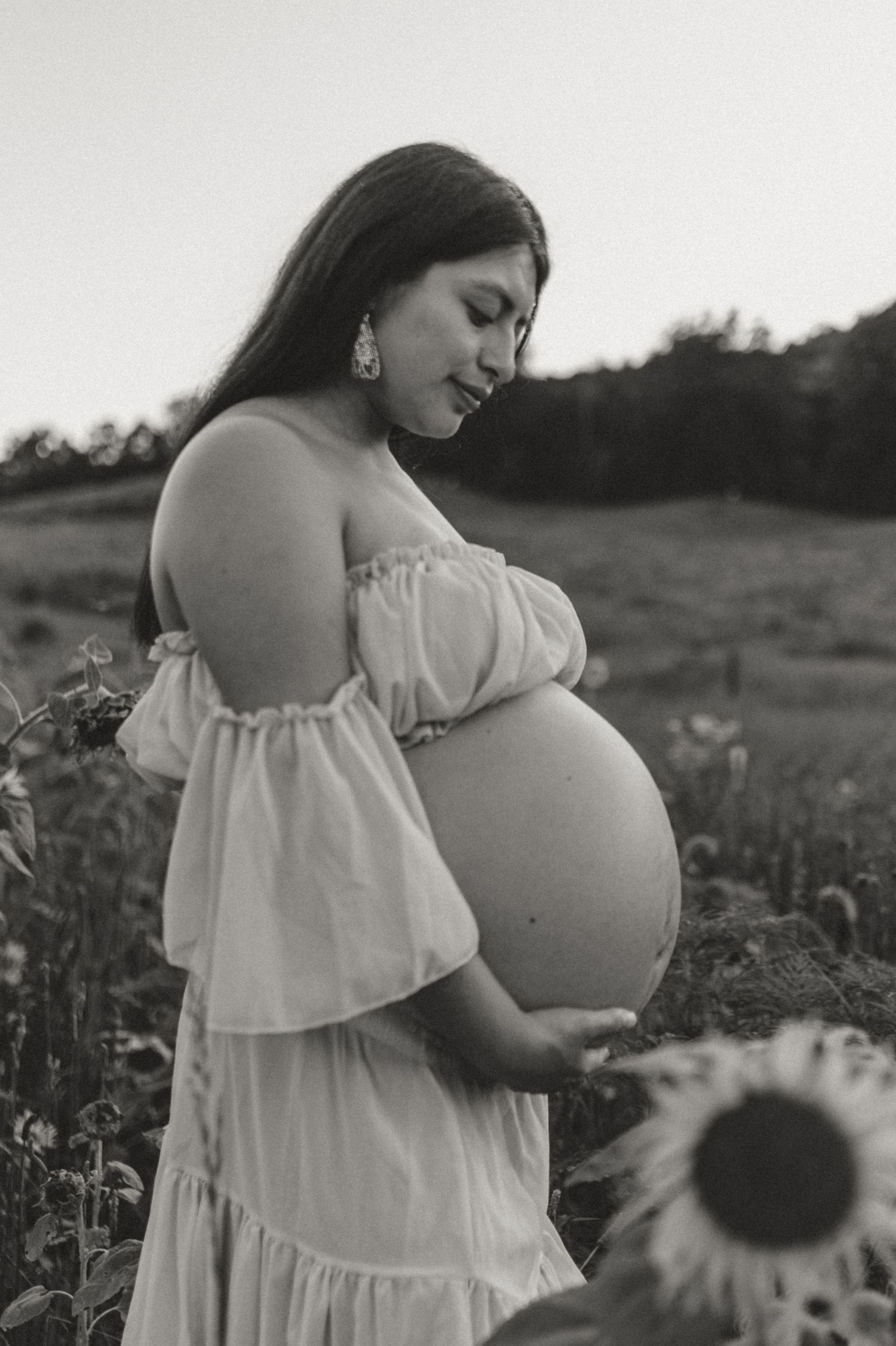 Itzayana looking down at belly in sunflower field at Fox Mountain Farms, Chattanooga, TN – maternity session, soft summer light