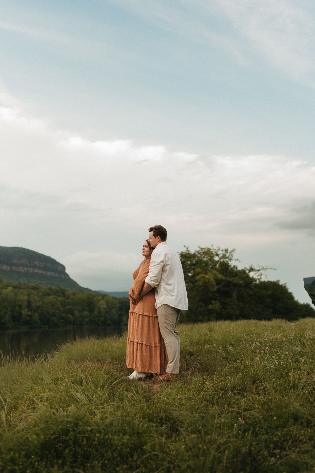 Expecting couple standing close in field with water and mountains behind them at maternity session at raccoon mountain, Chattanooga TN